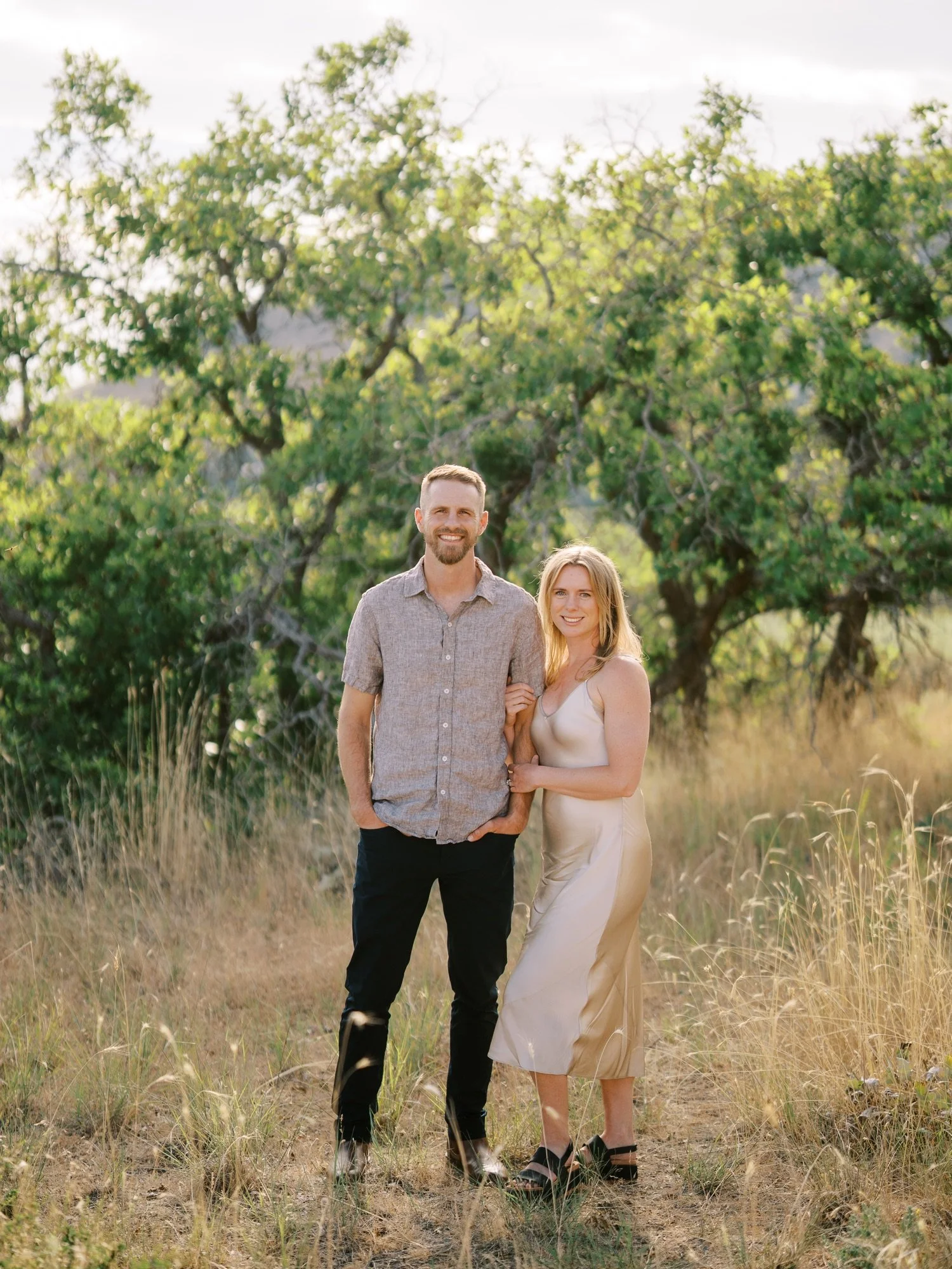 Engaged couple holding hands beside leafy green trees