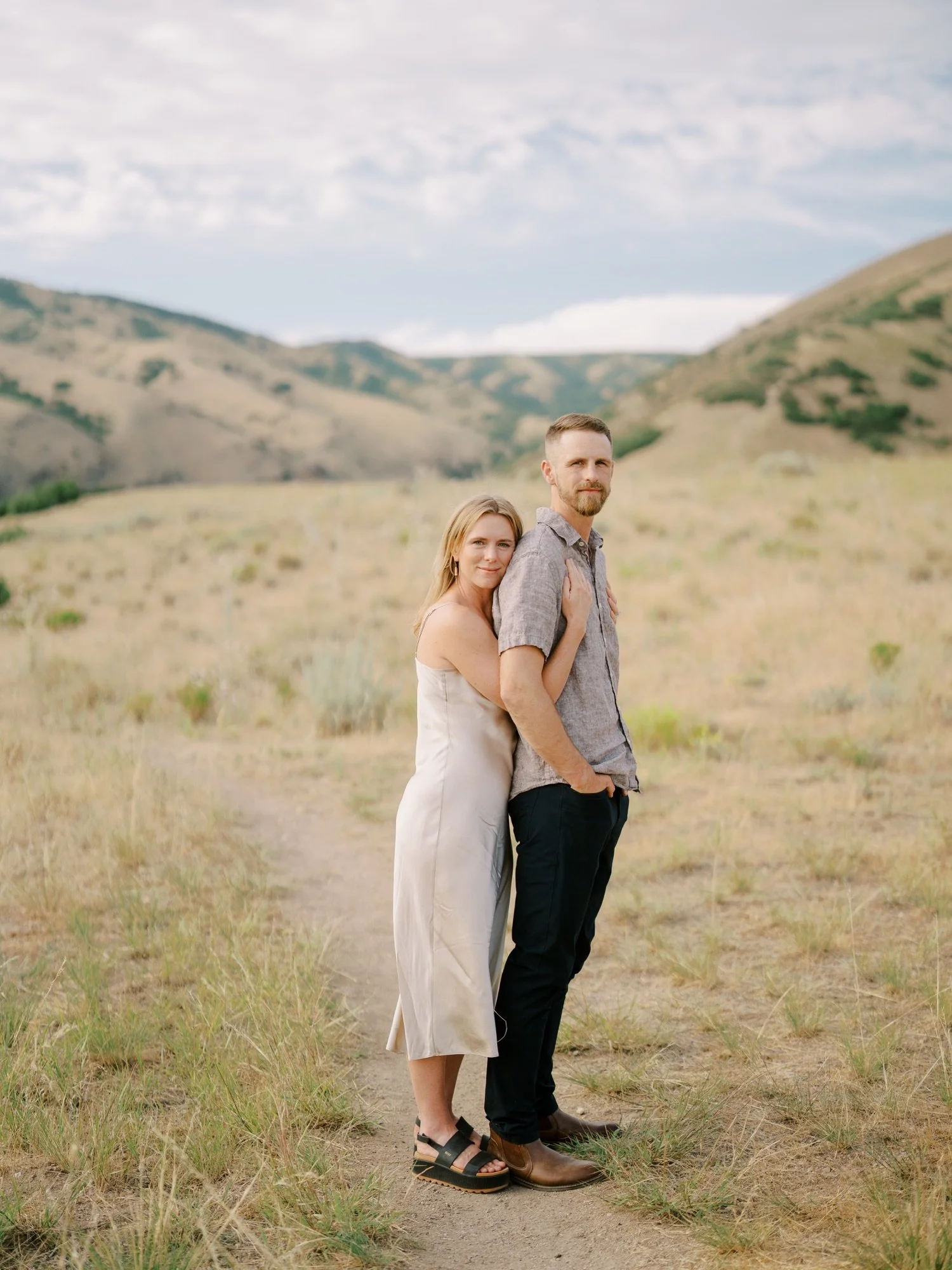 Engaged couple standing together with rolling hills behind them