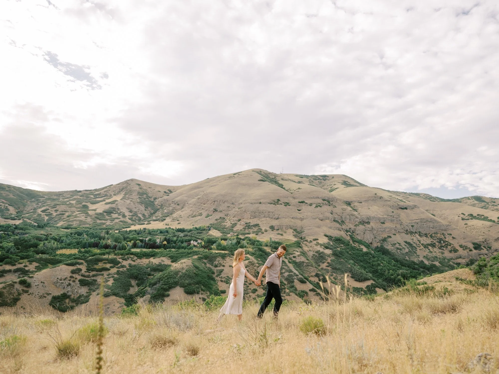 Couple walking across an open field beneath Northern Utah hills