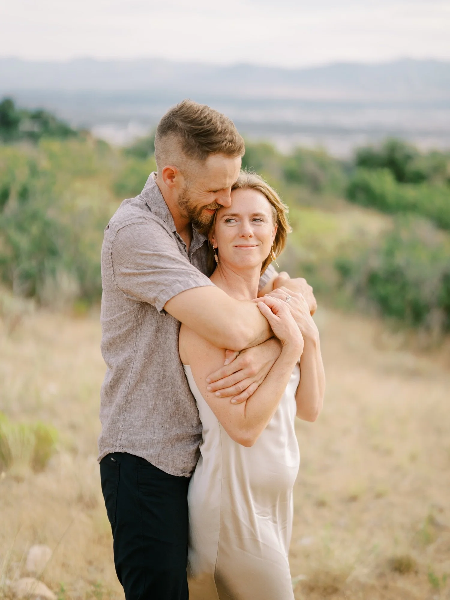 Couple cuddling in tall grass with mountains in the distance