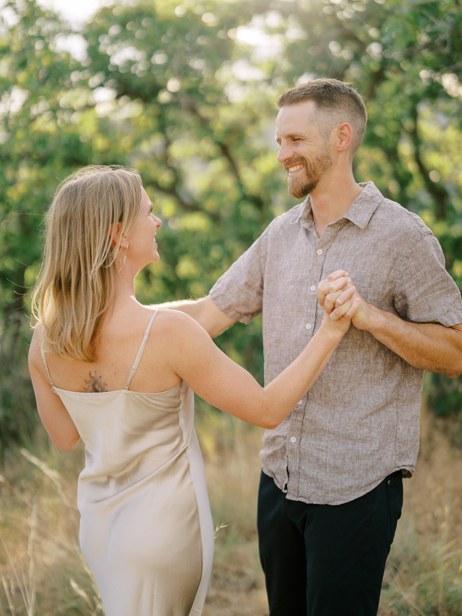 Couple holding hands and dancing beneath leafy trees