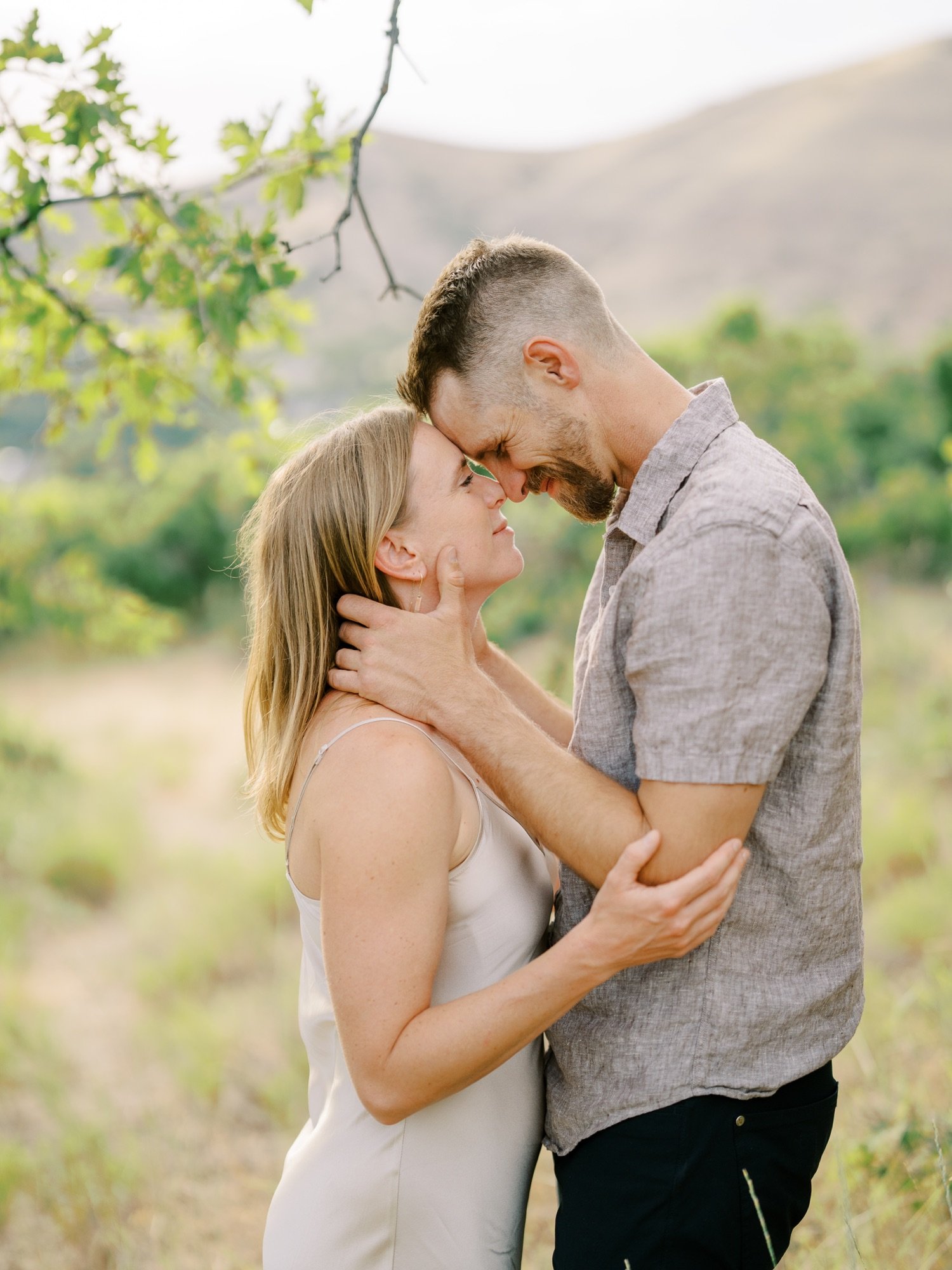 Couple leaning close together under green branches