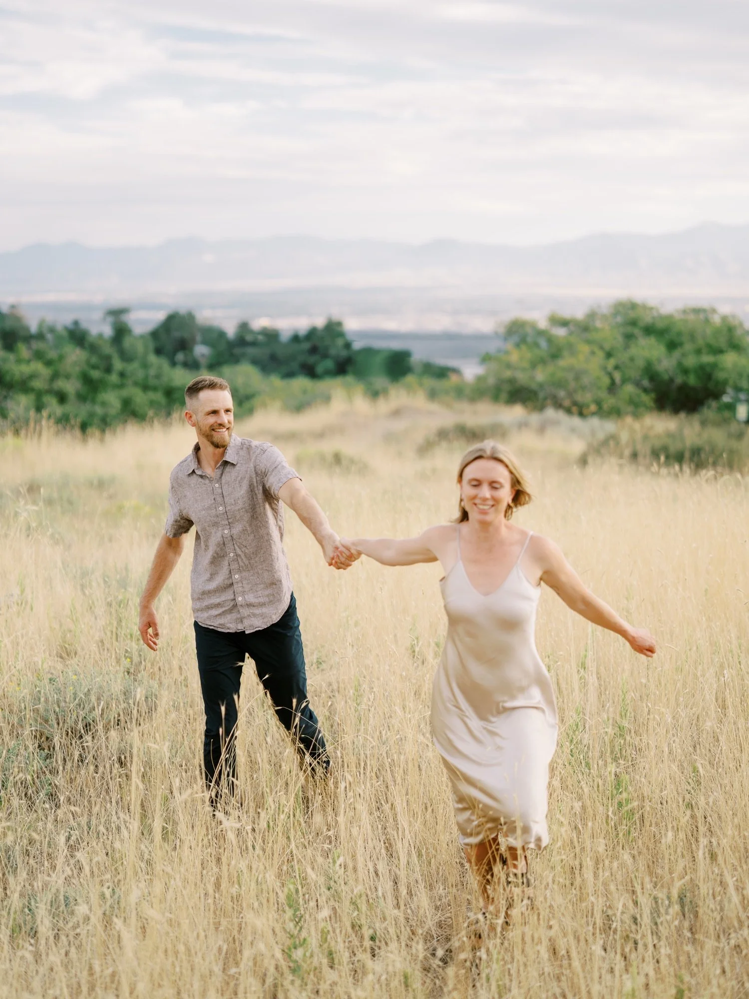 Couple running hand in hand through tall summer grass