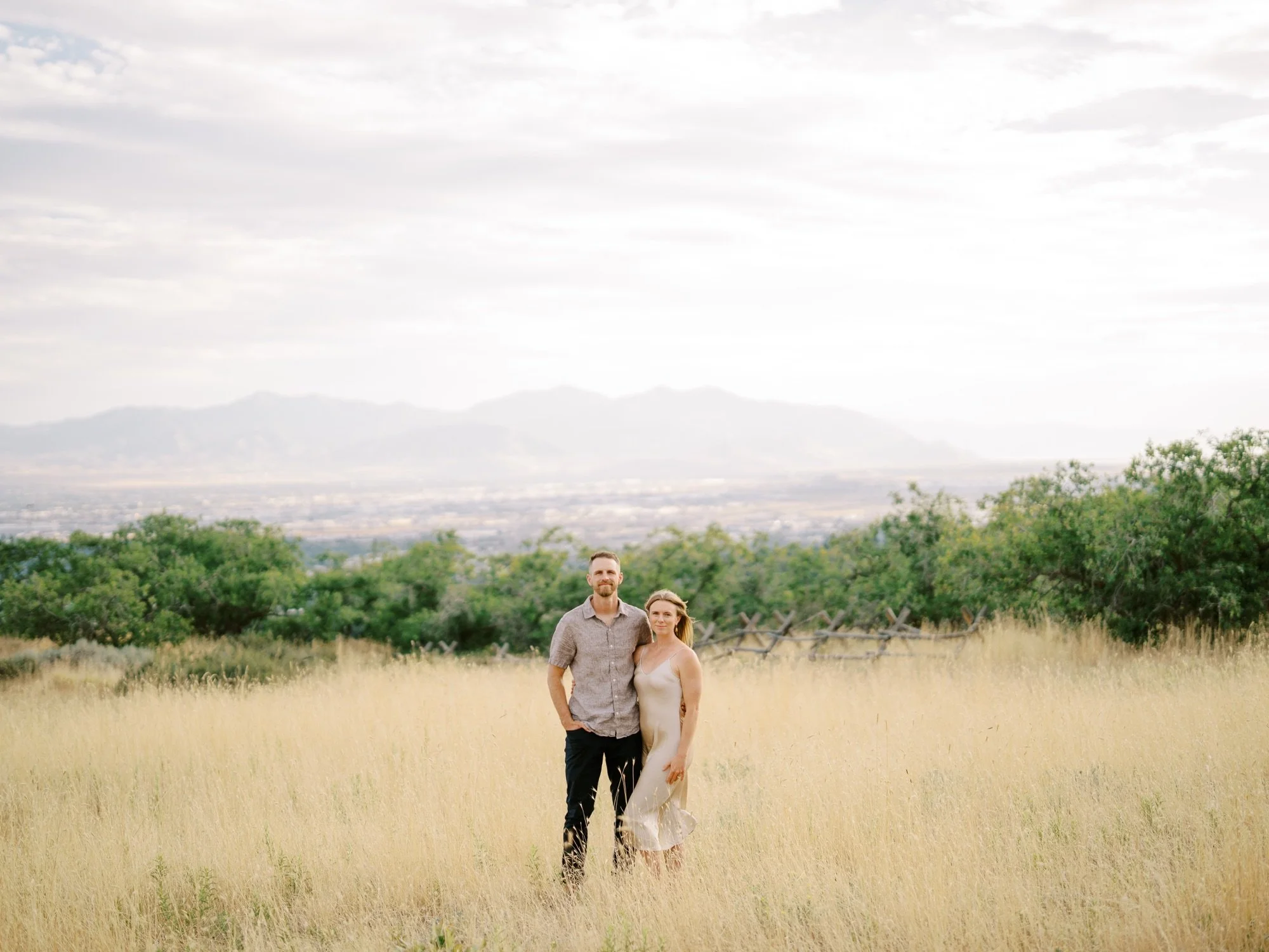Wide portrait of a couple standing in a meadow with distant mountain views