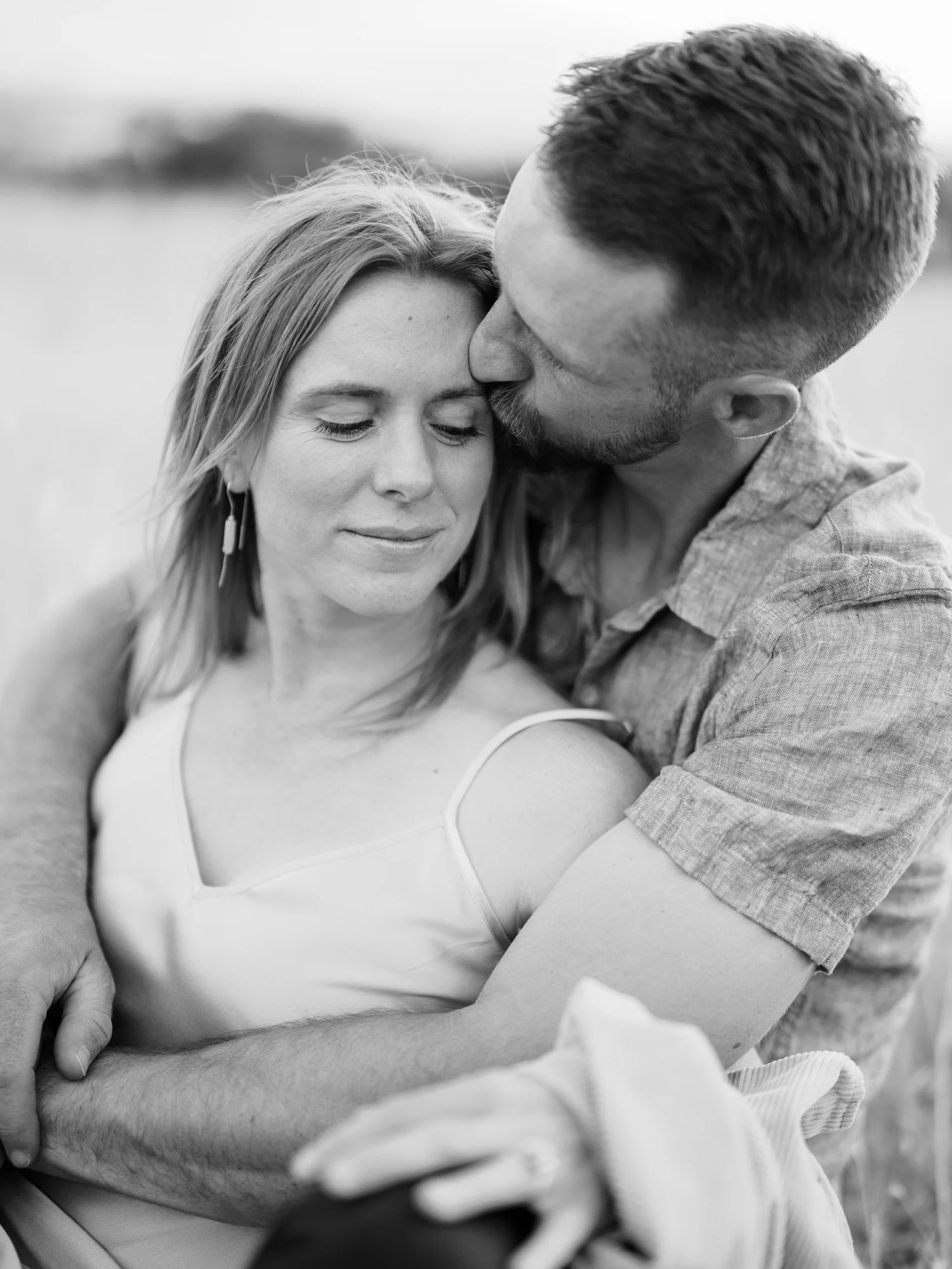 Black-and-white portrait of a man kissing his fiancée on the head