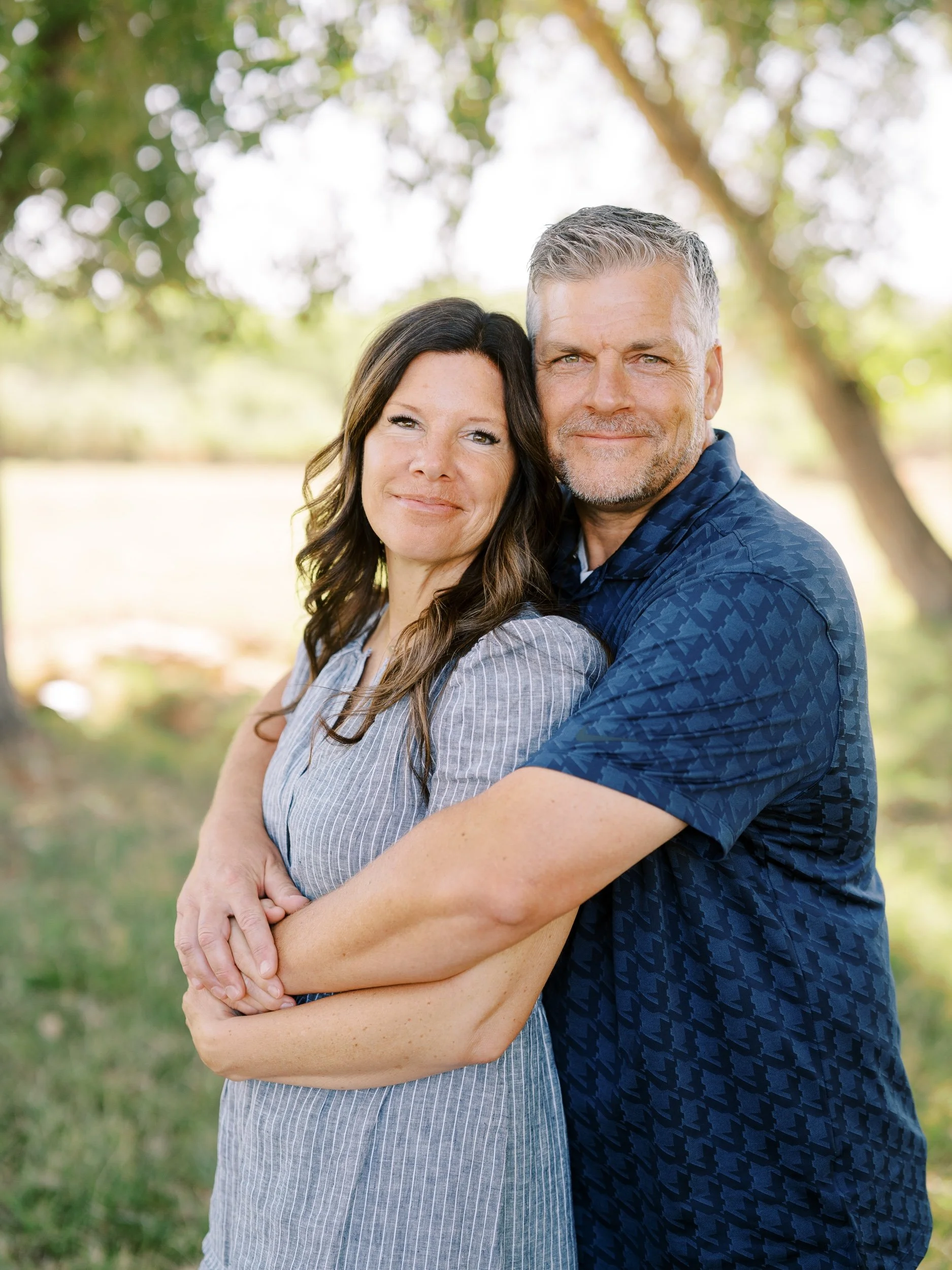 A couple embracing beneath the trees.