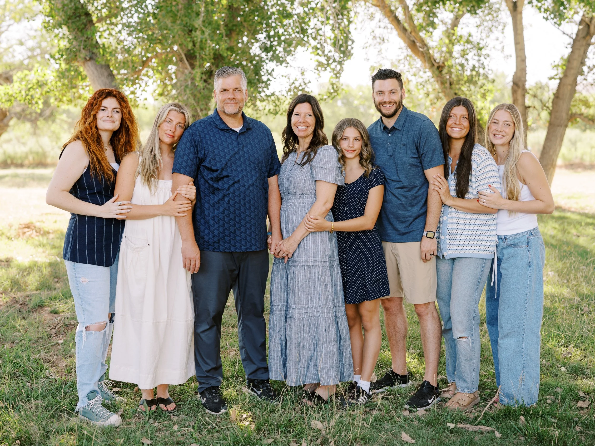 Adult family members standing together under leafy trees.