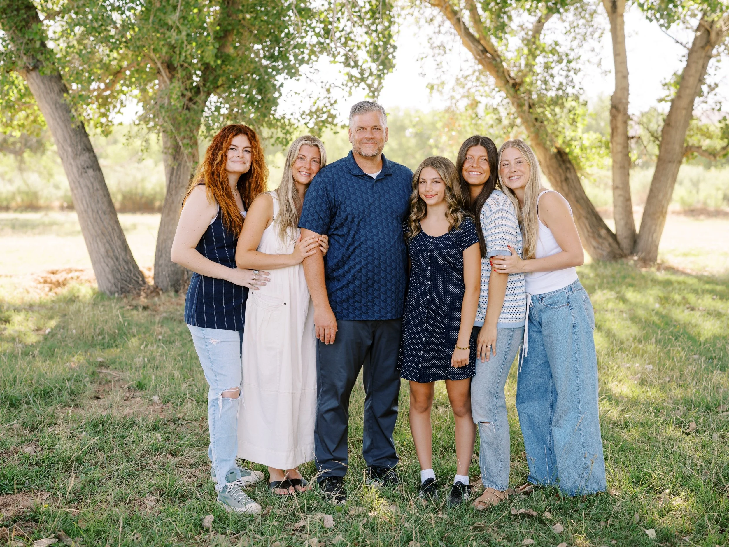 A man standing with five women beneath the trees.
