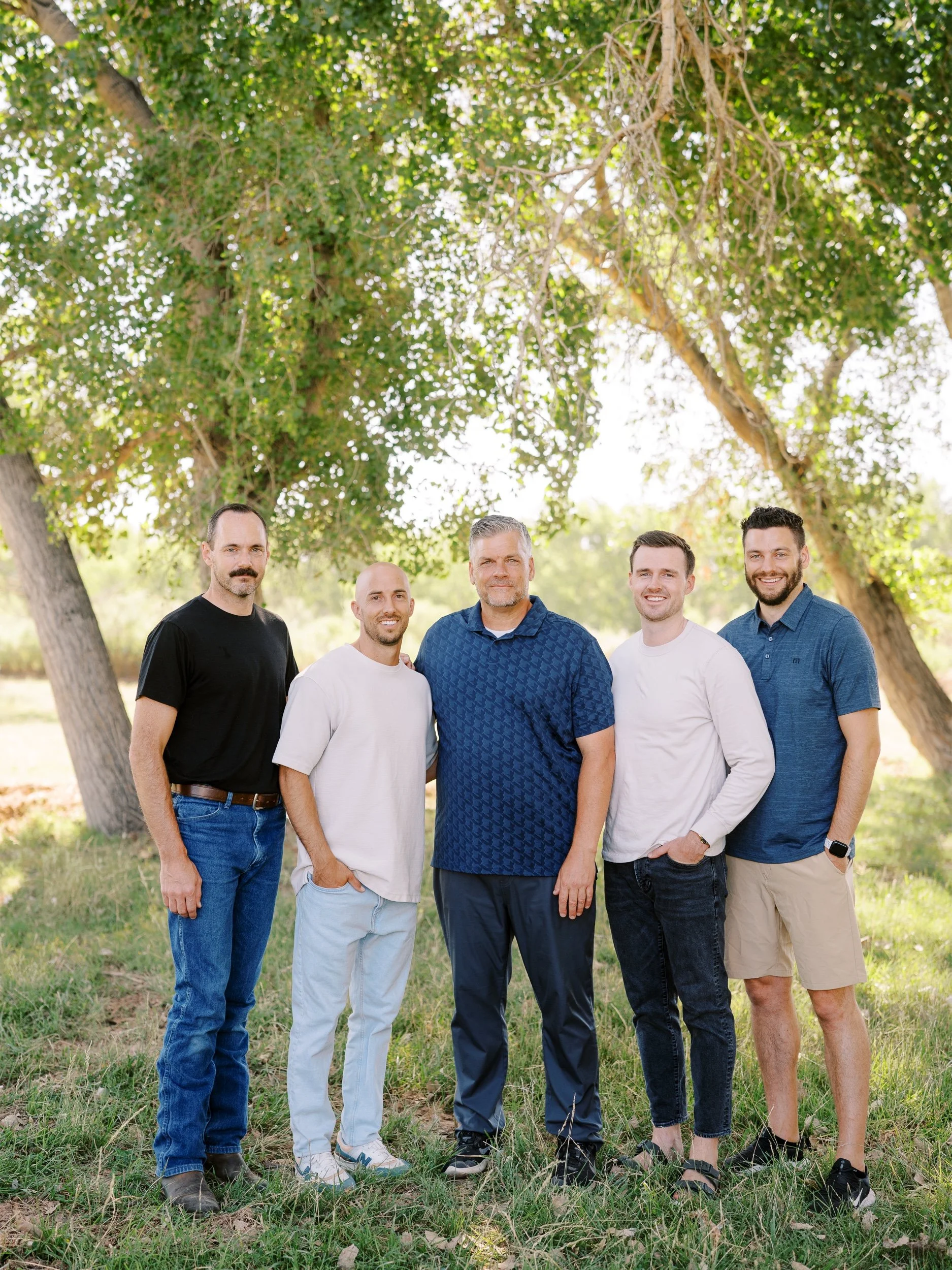 Five men standing side by side beneath the trees.