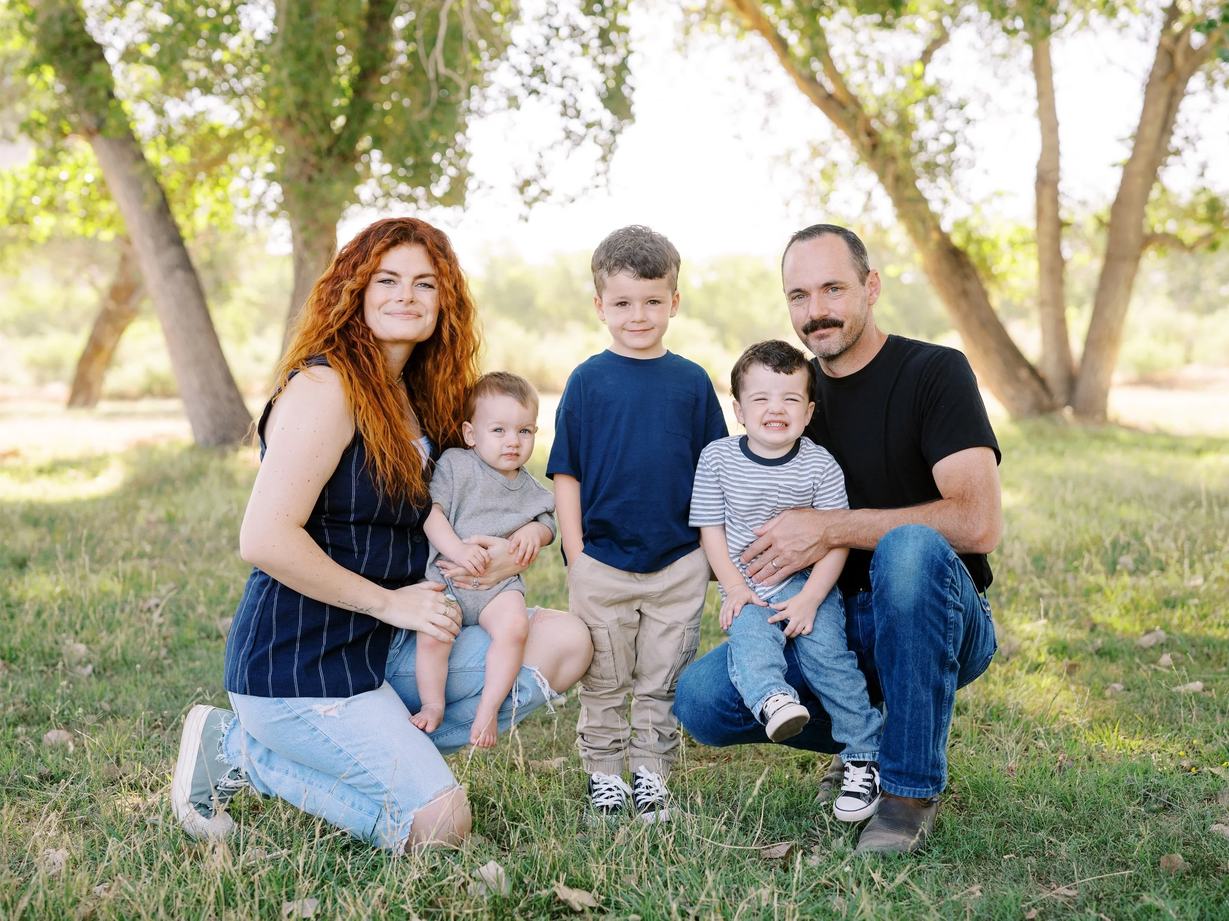 Parents kneeling on the grass with their three young children.