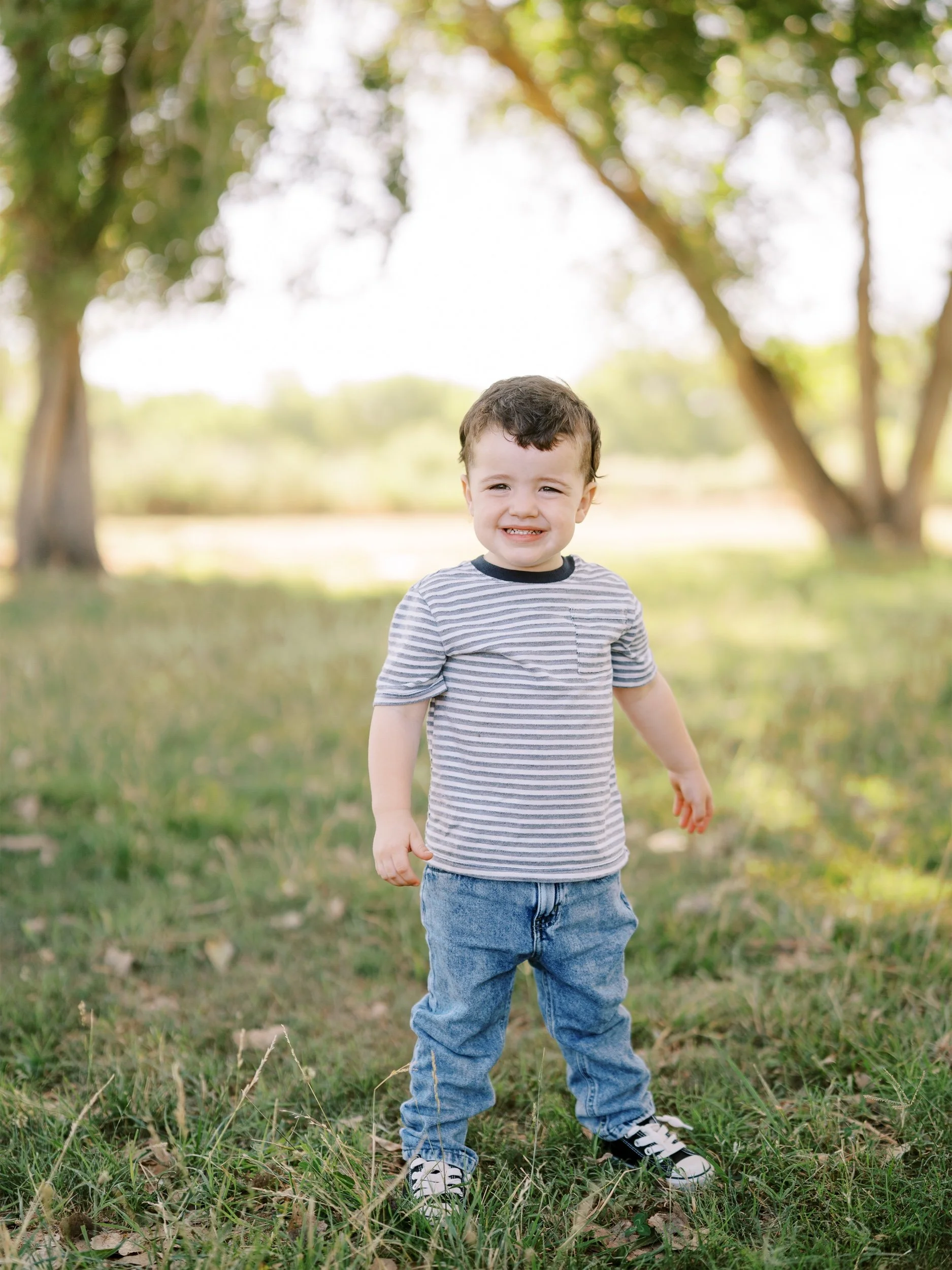 A young boy in a striped shirt standing on the grass.