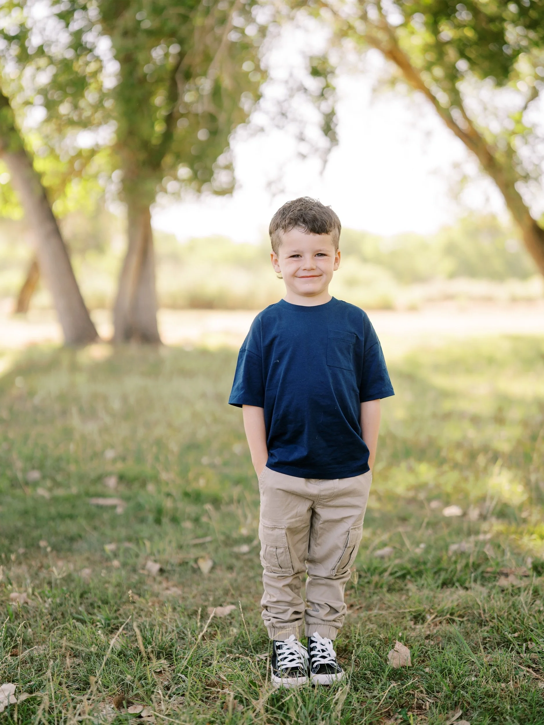 A boy in a navy shirt smiling beneath the trees.