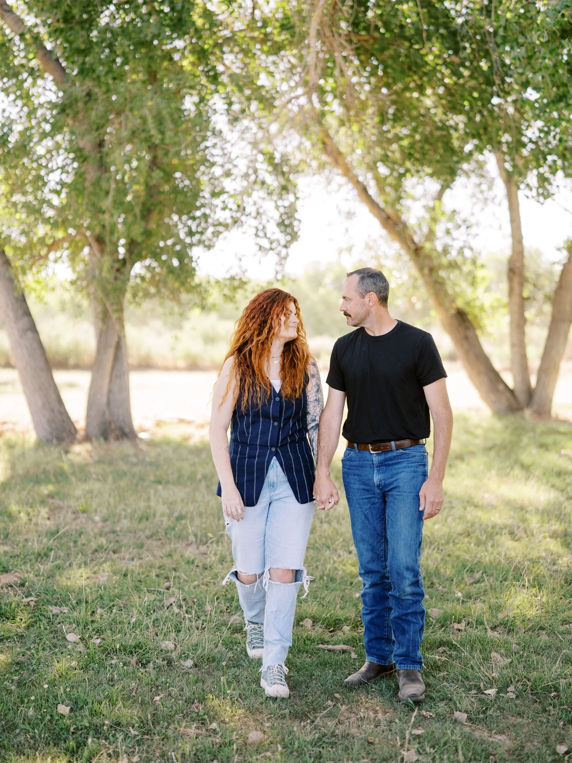 A couple walking hand in hand beneath the trees.