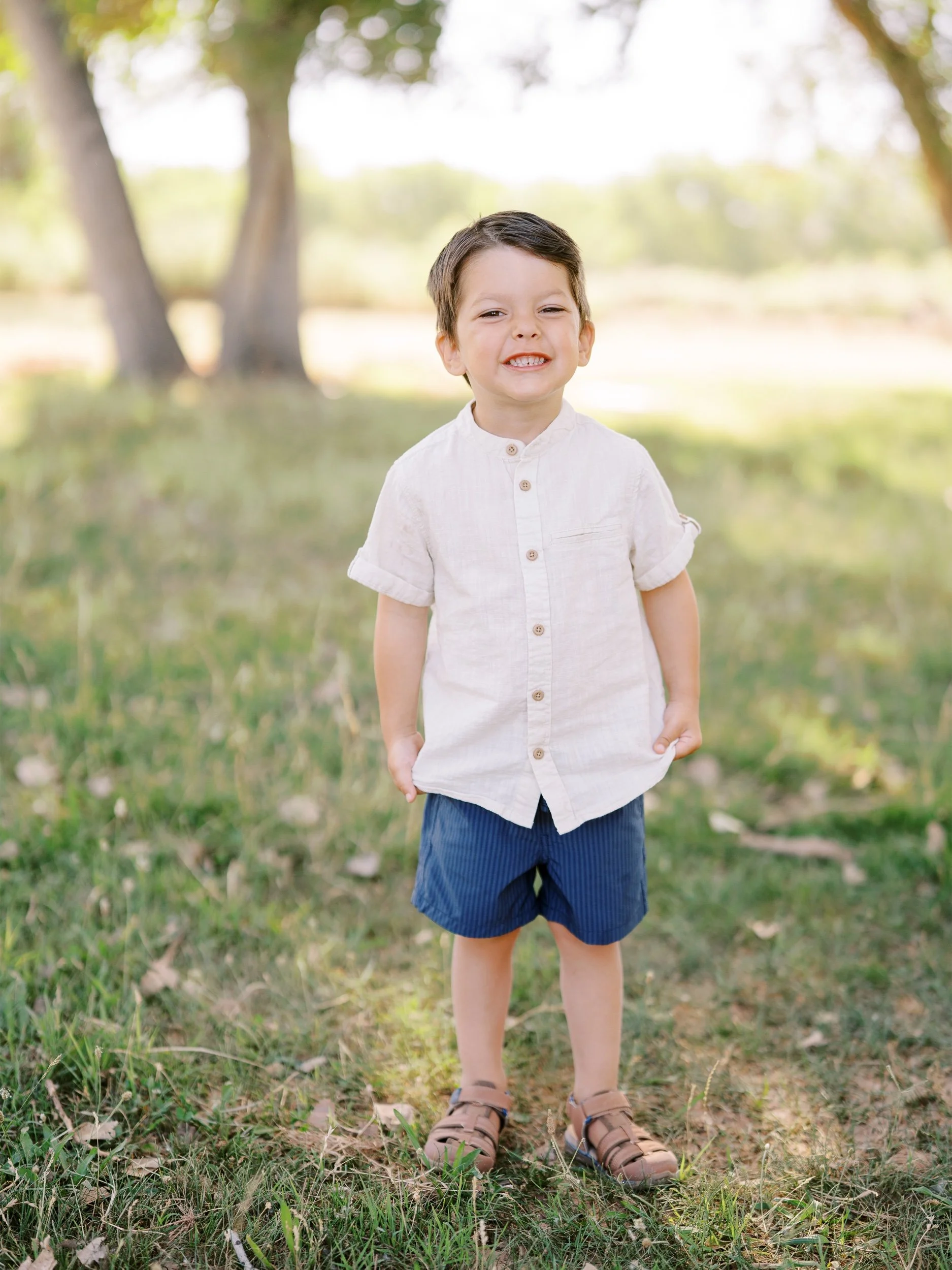 A boy in a cream shirt standing on the grass.