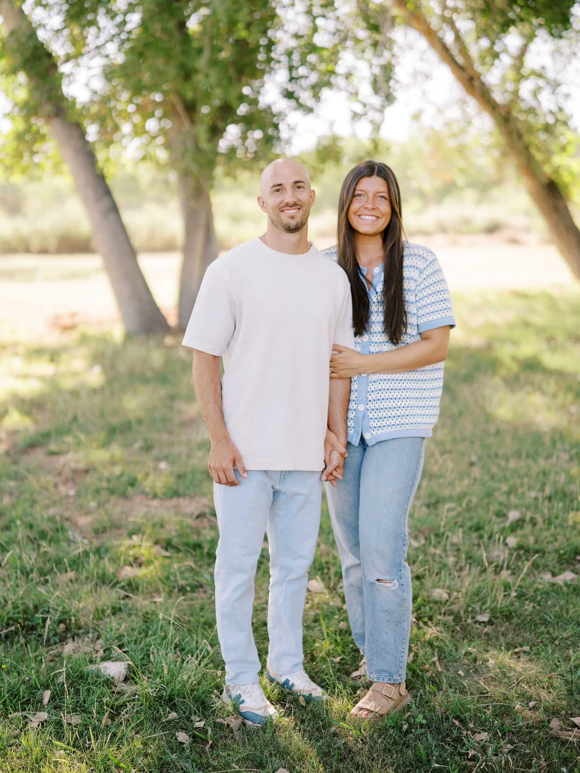 A couple standing together under the trees.