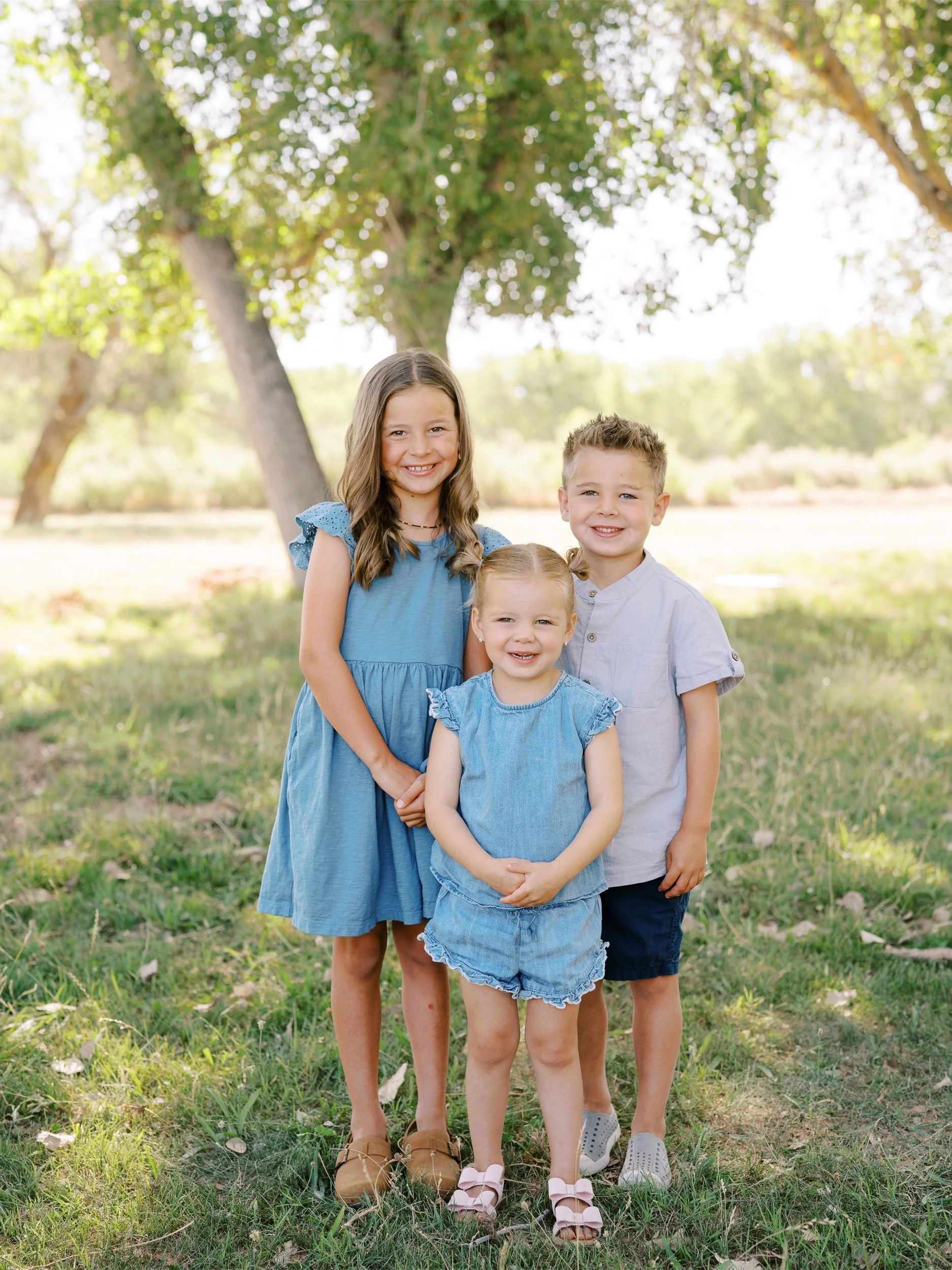 Three siblings standing together in blue outfits.