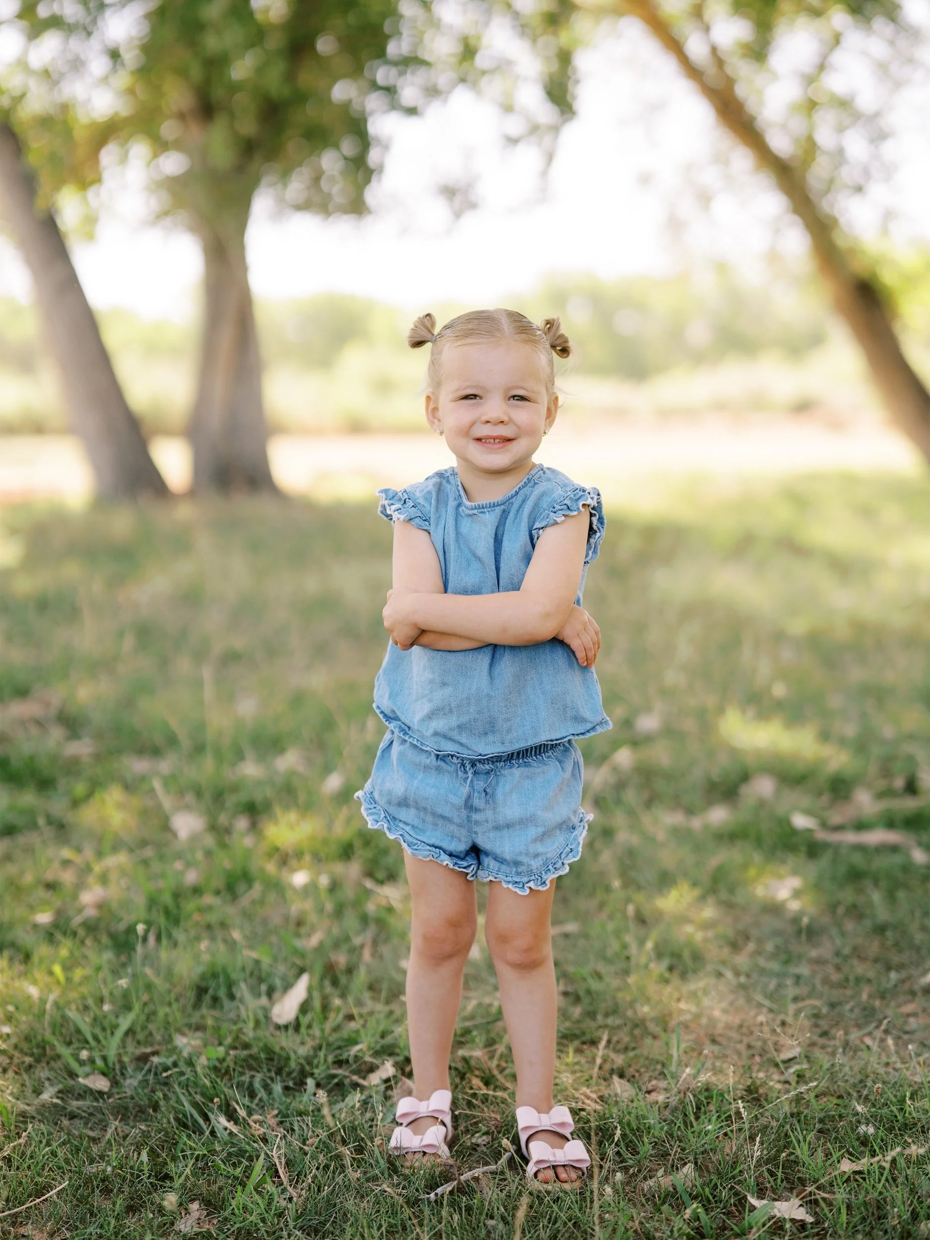 A little girl in a blue ruffled outfit with her arms crossed.