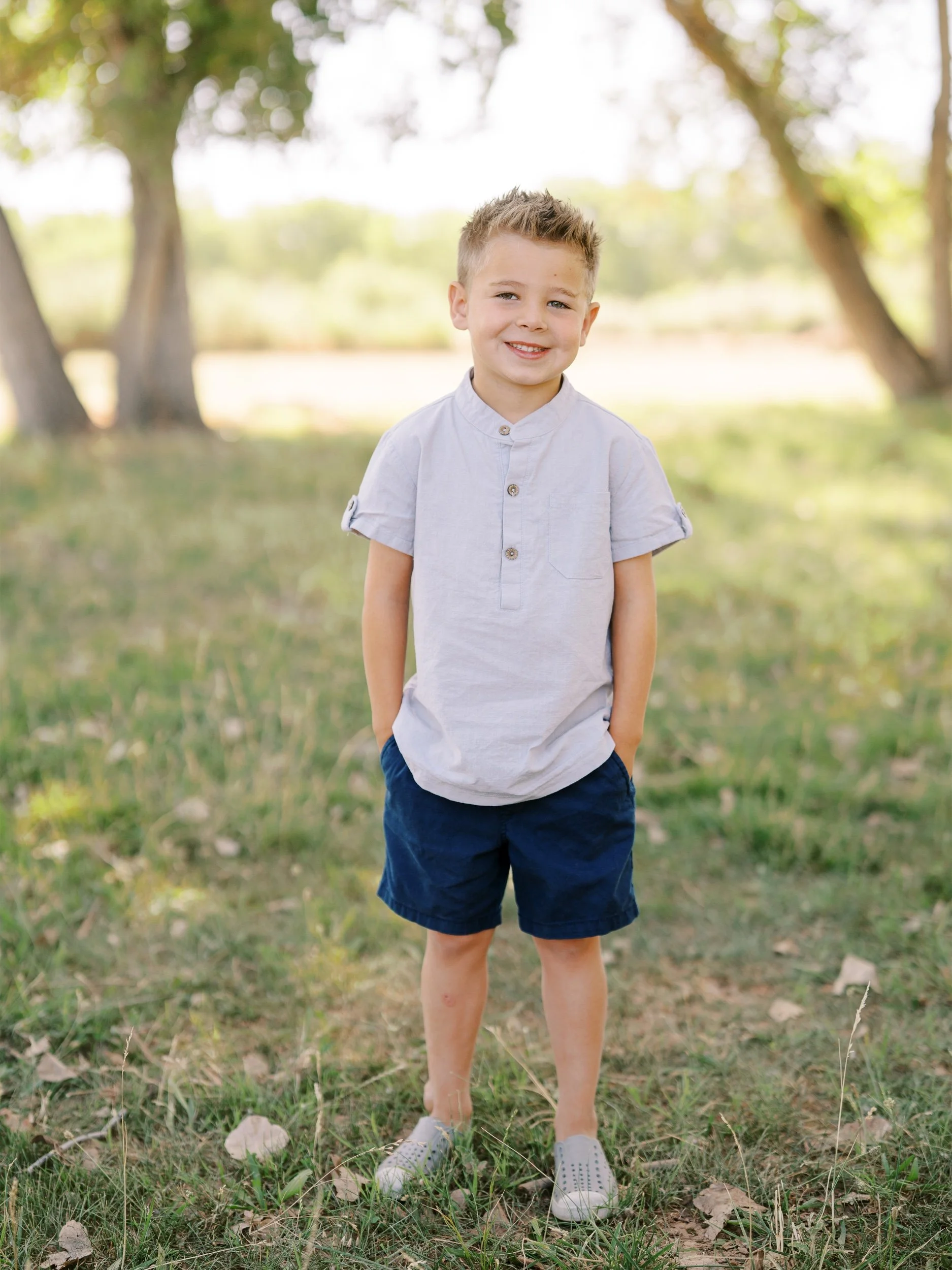 A smiling boy in a pale shirt and navy shorts.