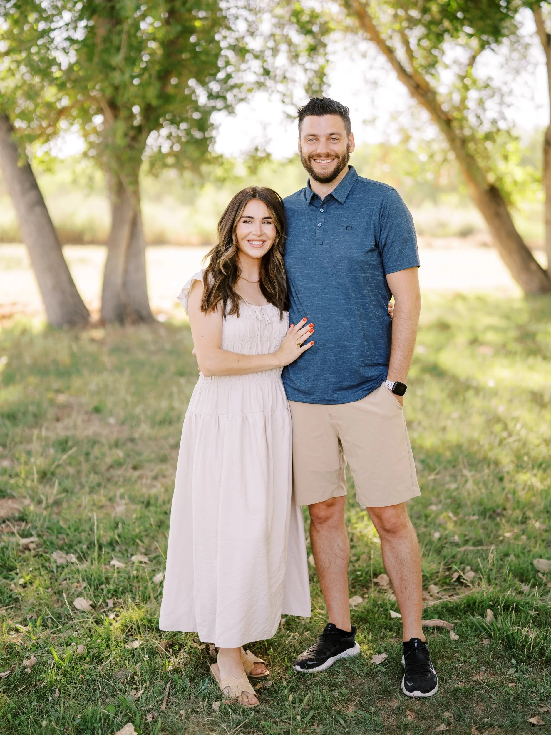 A couple standing together, wearing a cream dress and navy shirt.