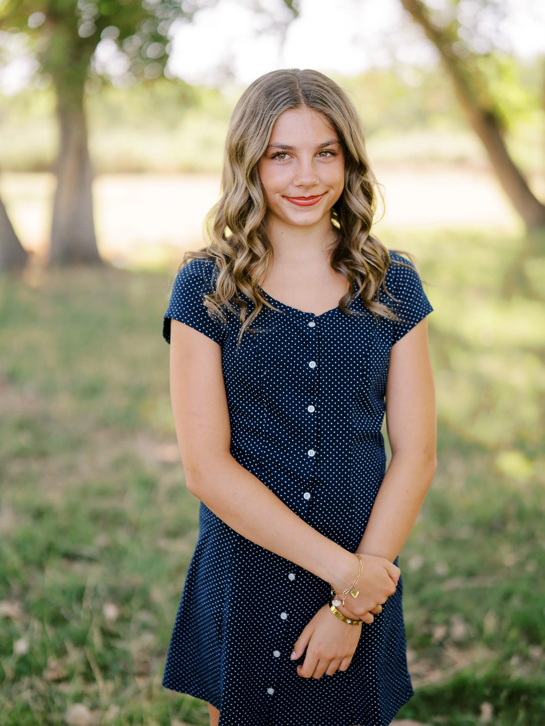 A girl in a navy dotted dress smiling at the camera.