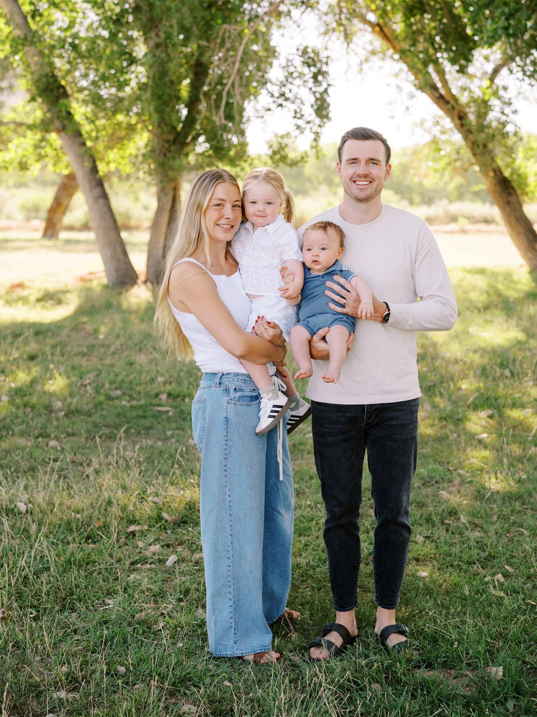 Parents holding their two young children beneath the trees.