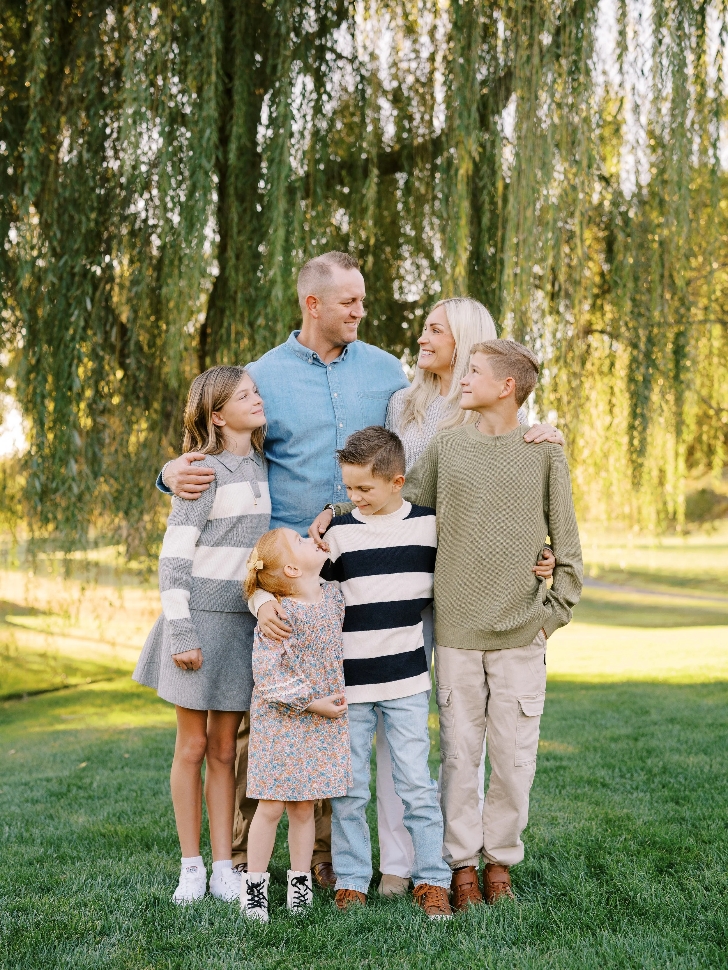 Family gathered beneath a willow, smiling and looking at one another
