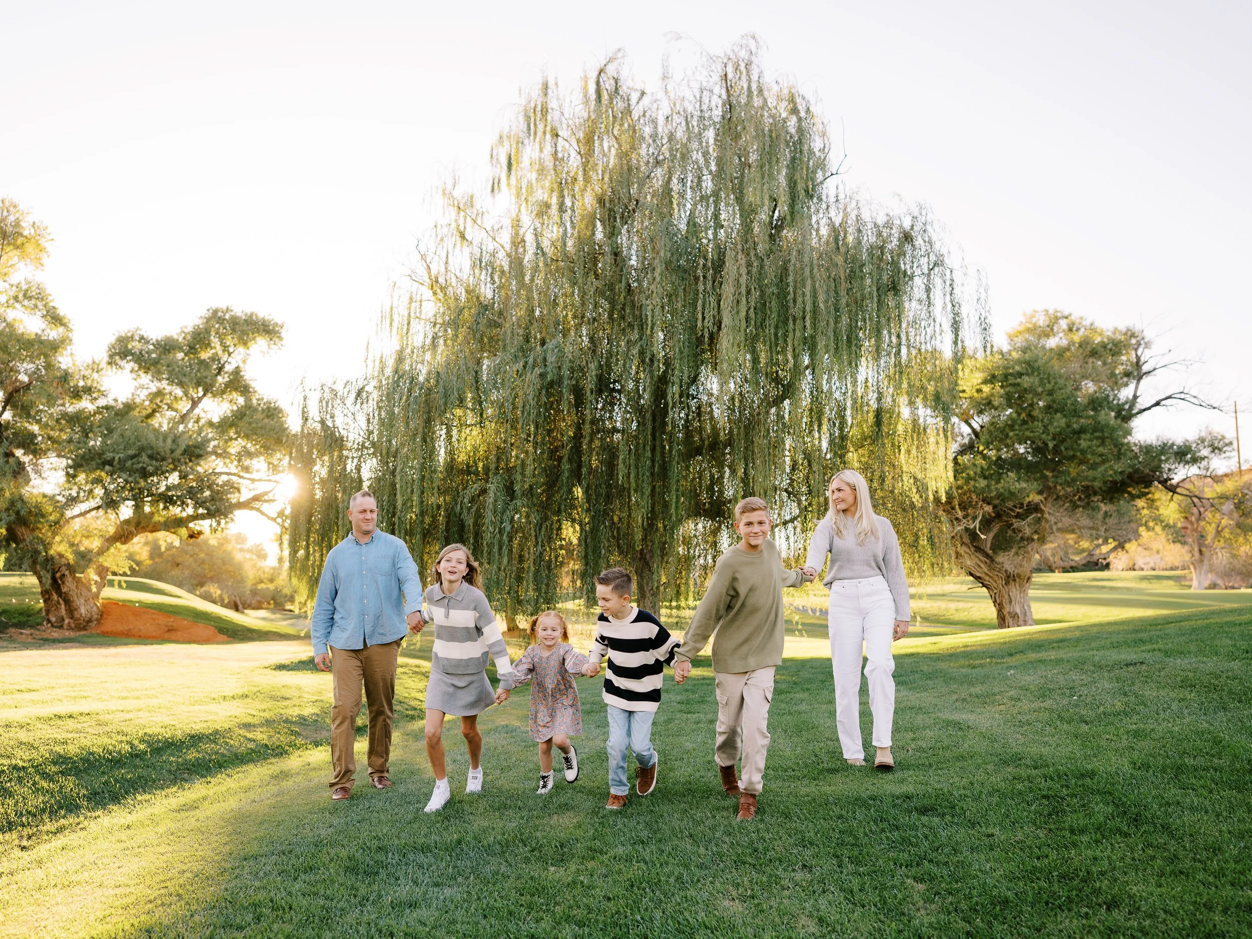 Family holding hands and walking across the grass with a willow behind them