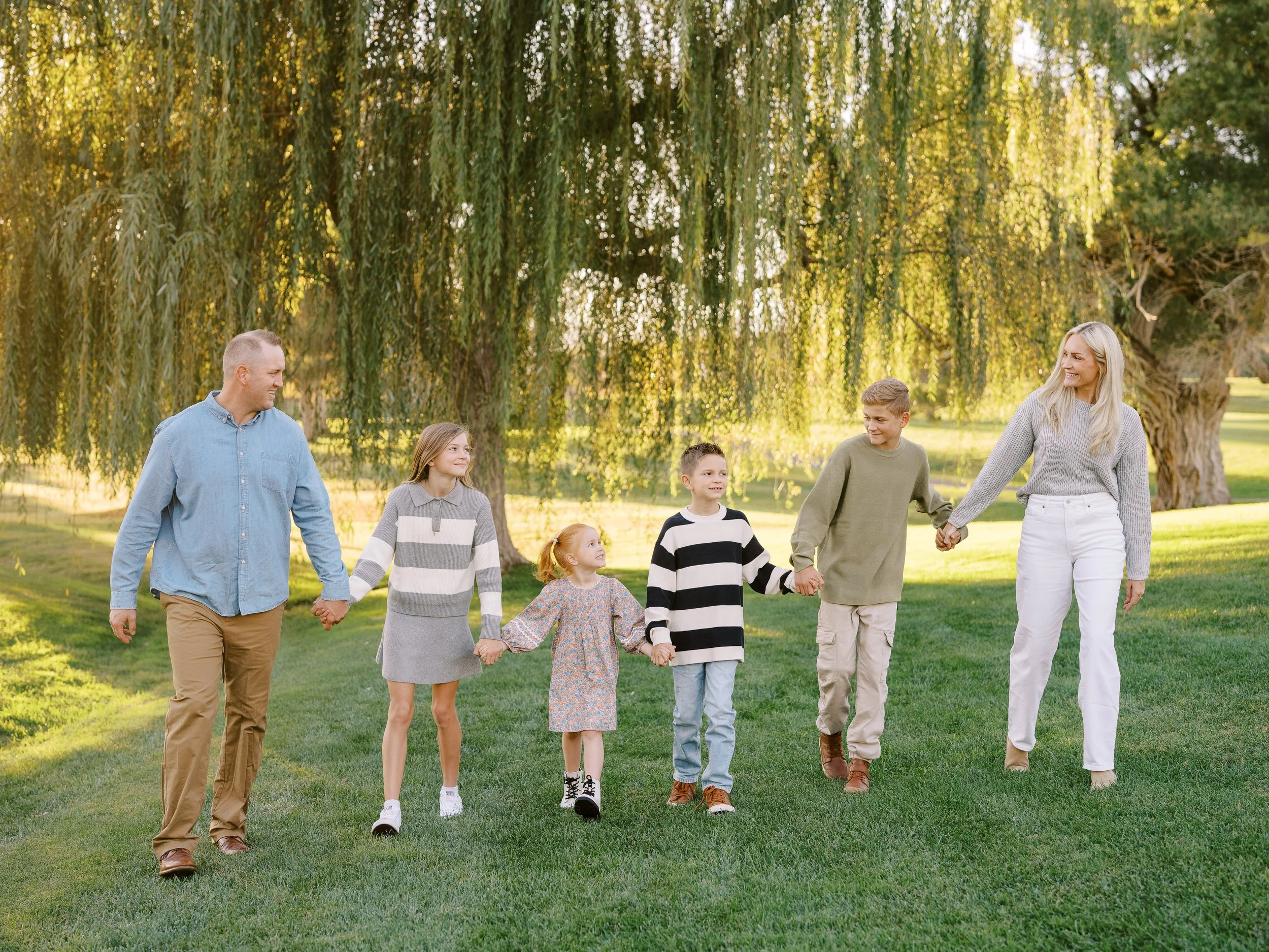 Parents and children walking hand in hand beneath a willow tree