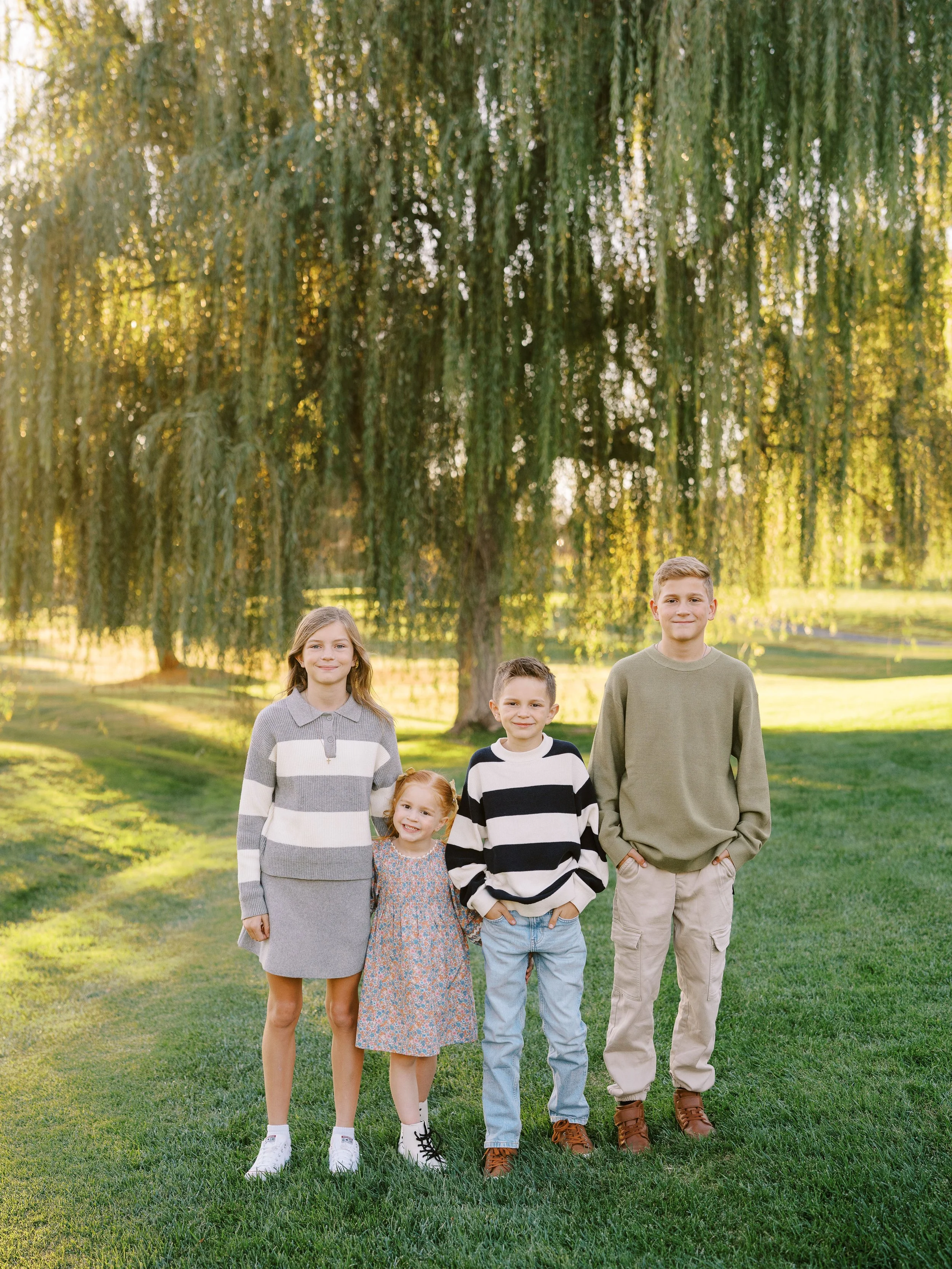 Four siblings standing together on the grass beneath hanging branches