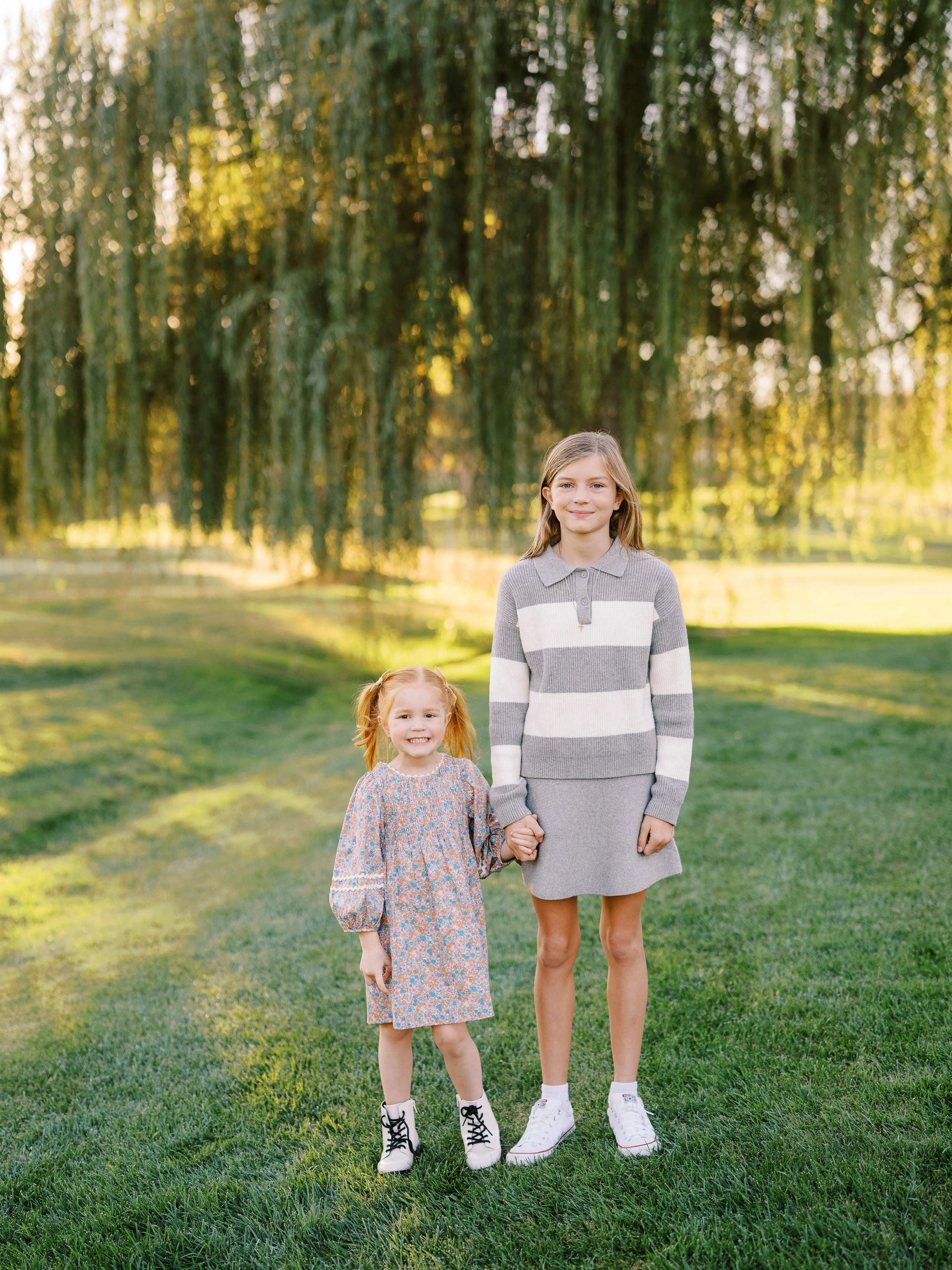 Two sisters holding hands on the grass beneath the willow