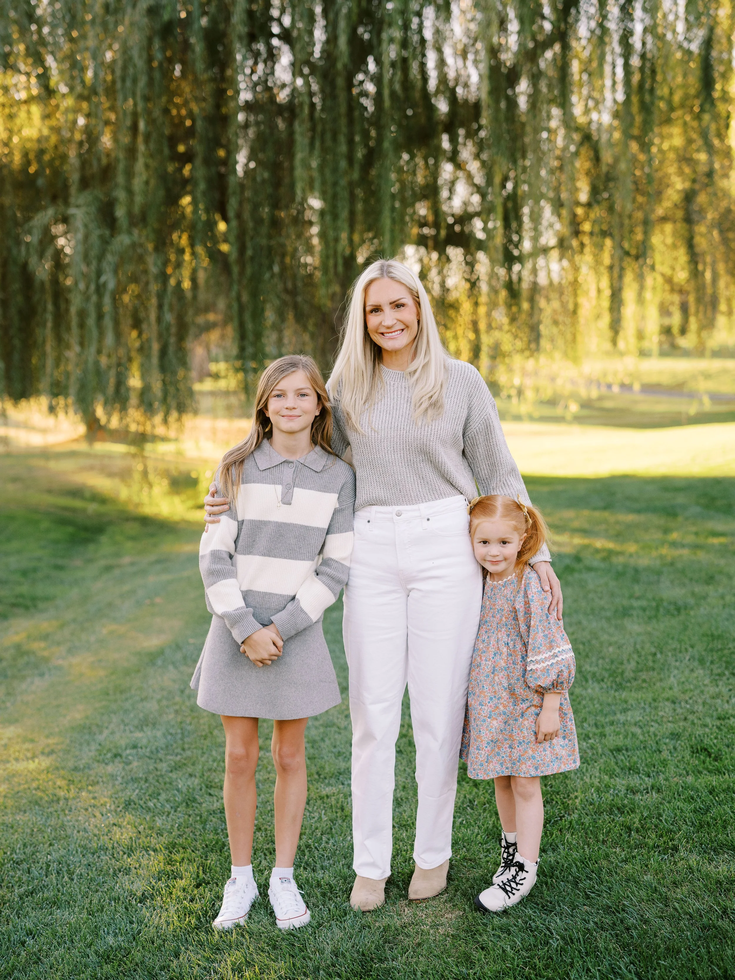 Mother standing with her two daughters beneath hanging willow branches
