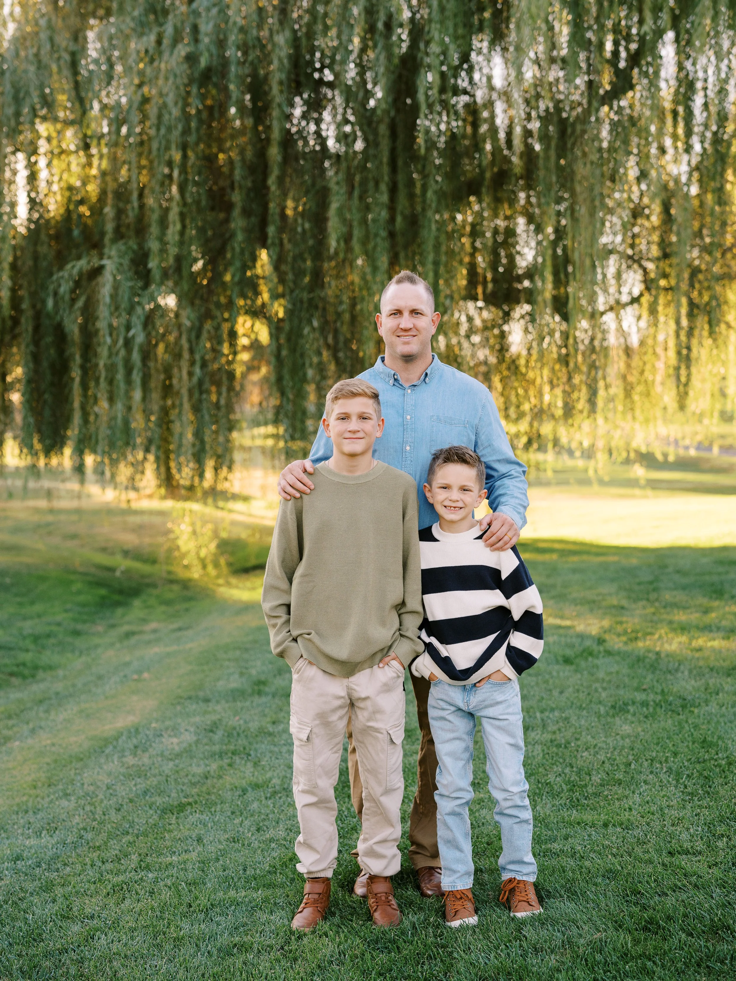 Father smiling with his two sons beneath a willow tree