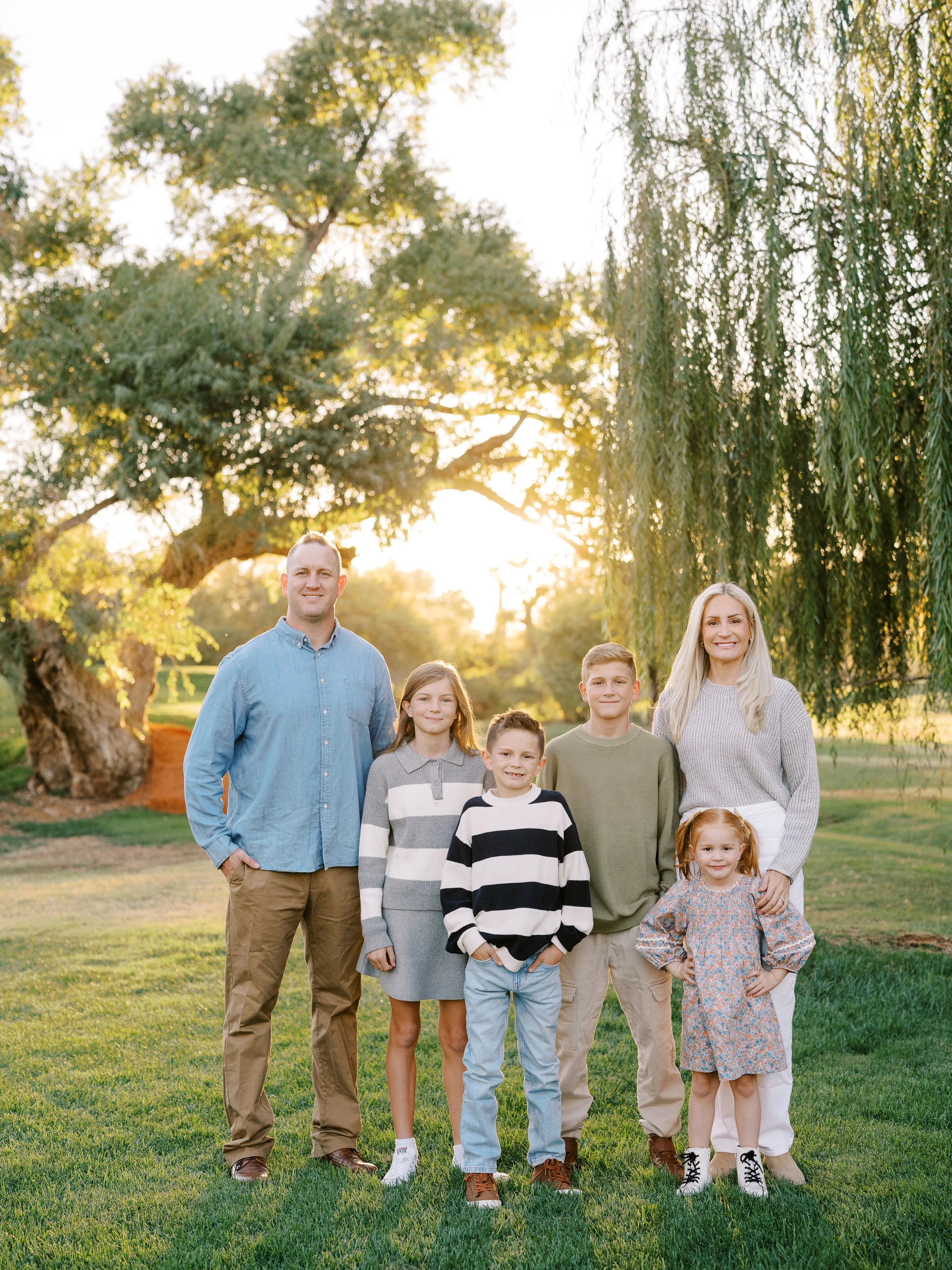 Family of six standing together with sunlit trees behind them