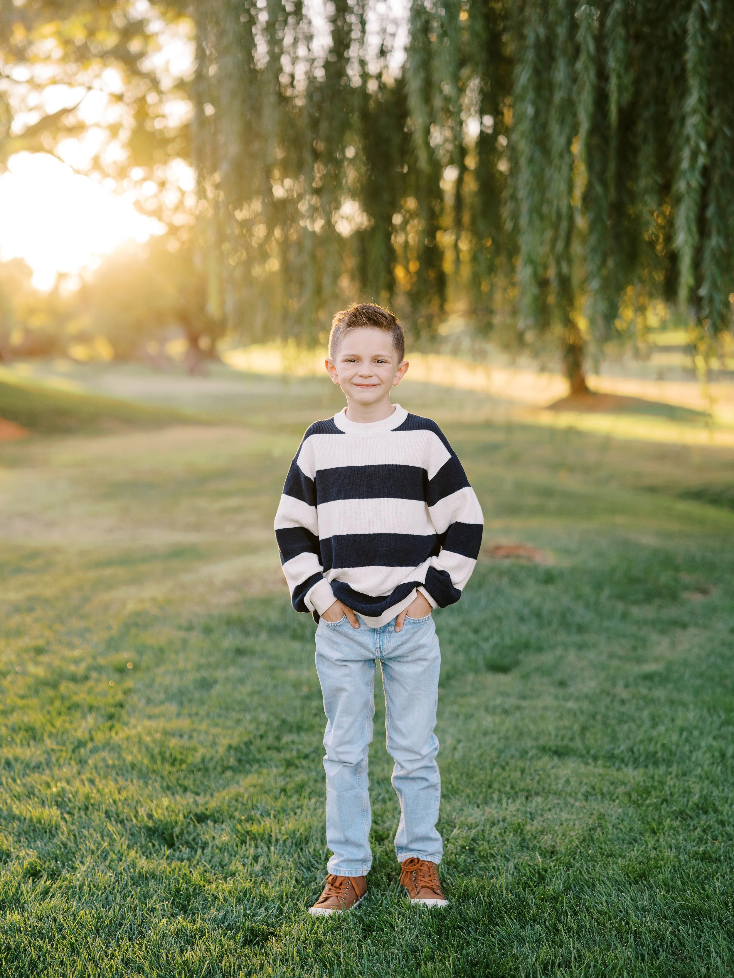Boy in a navy and cream striped sweater standing on the grass