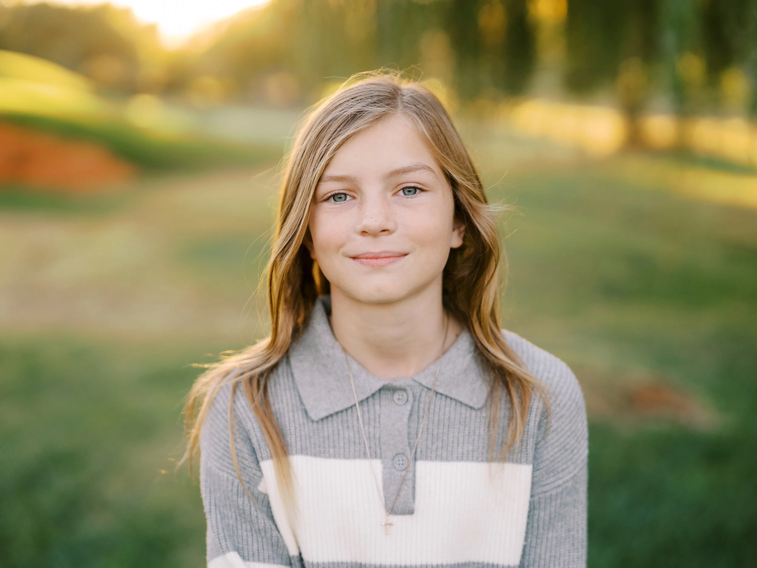 Close portrait of a smiling girl with softly blurred trees behind her