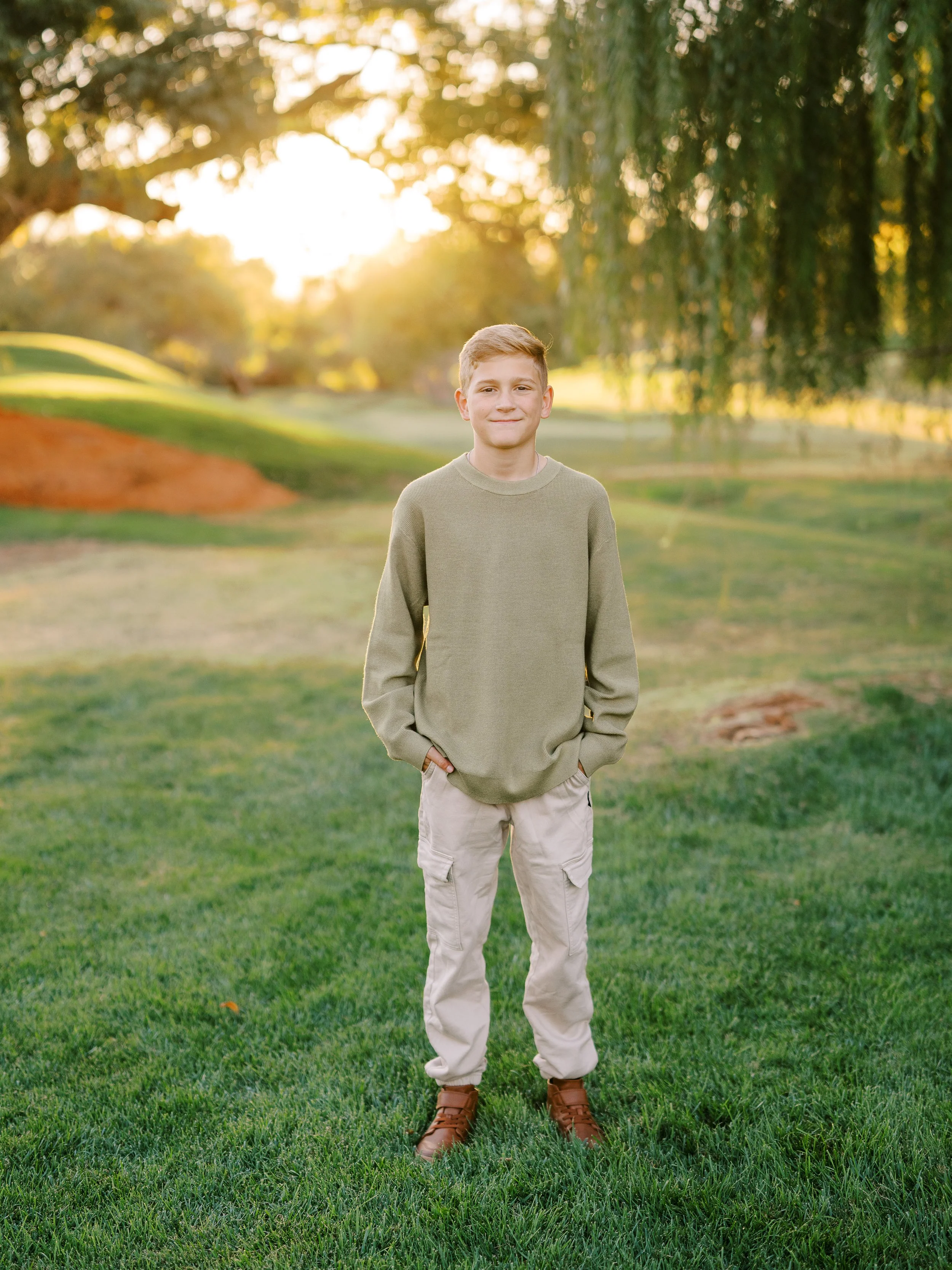 Boy in an olive sweater and light trousers standing on the lawn