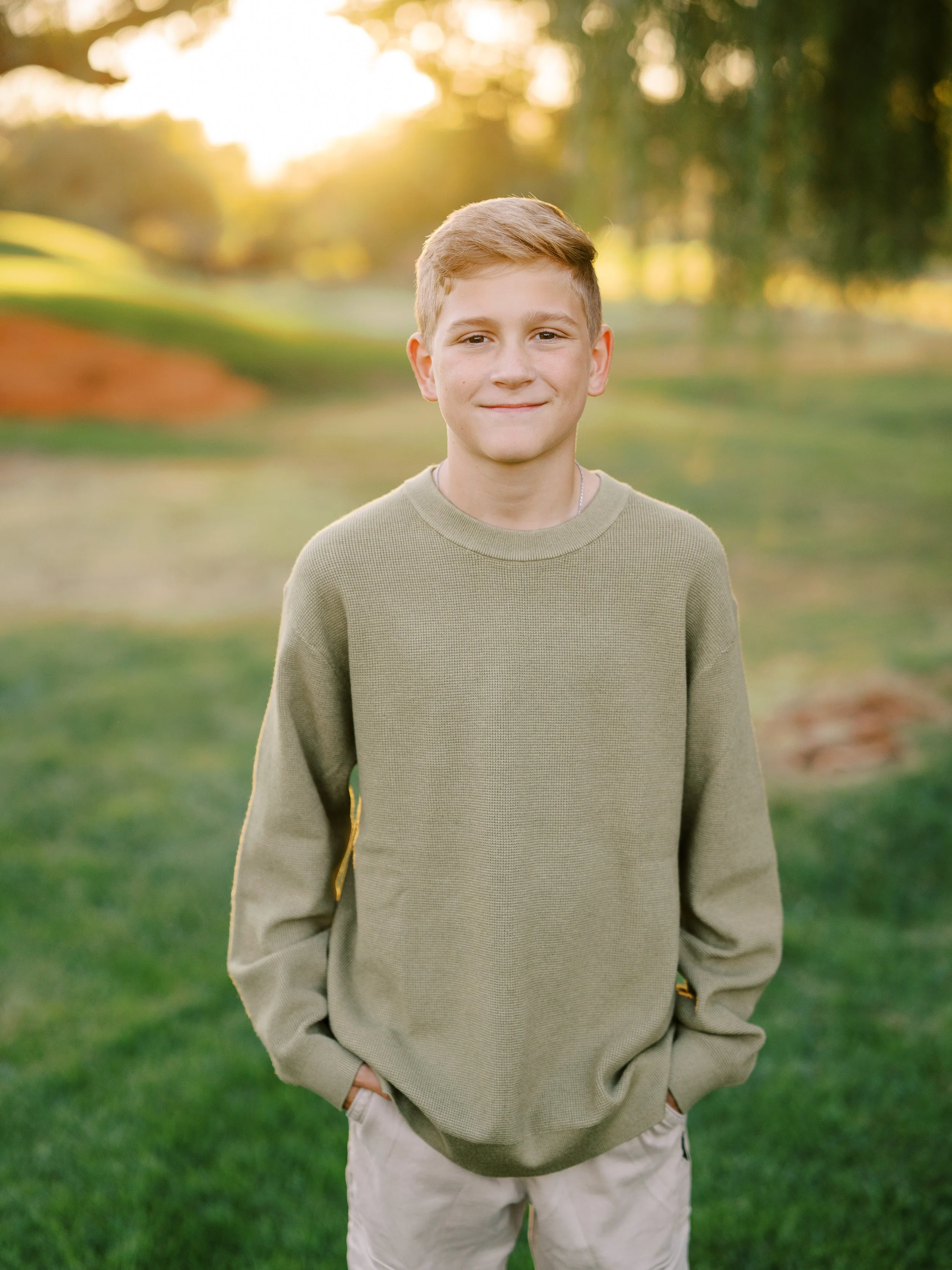 Portrait of a boy in an olive sweater with warm evening light behind him