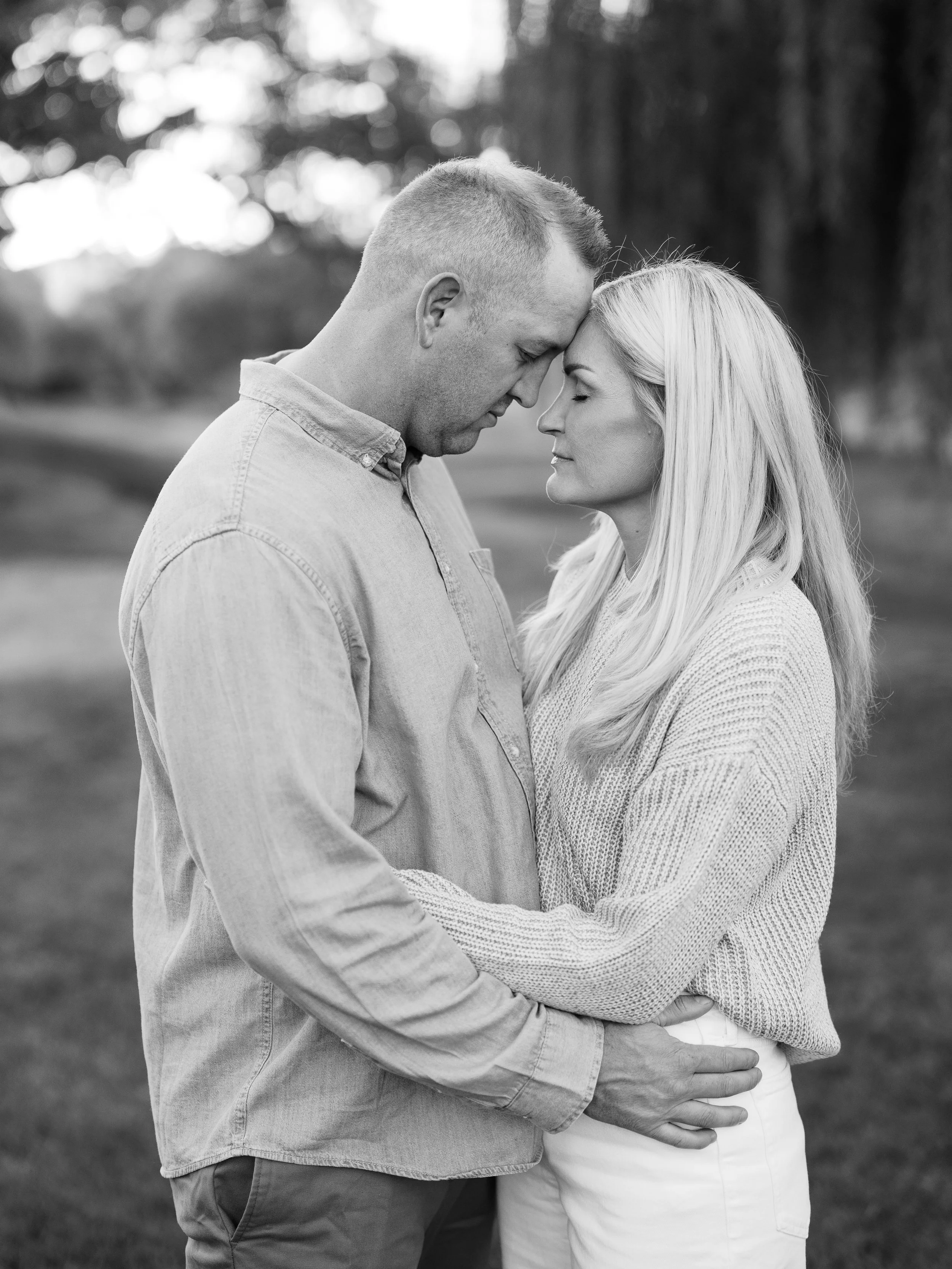 Black and white portrait of a couple kissing beneath the trees