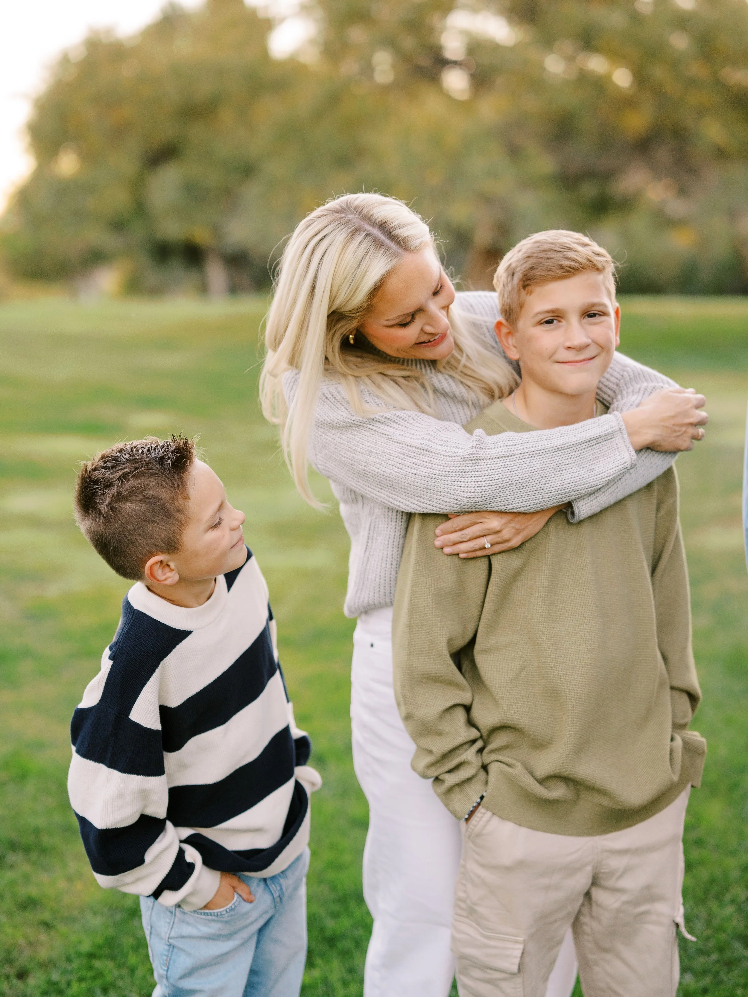 Mother hugging her older son while her younger son smiles beside them