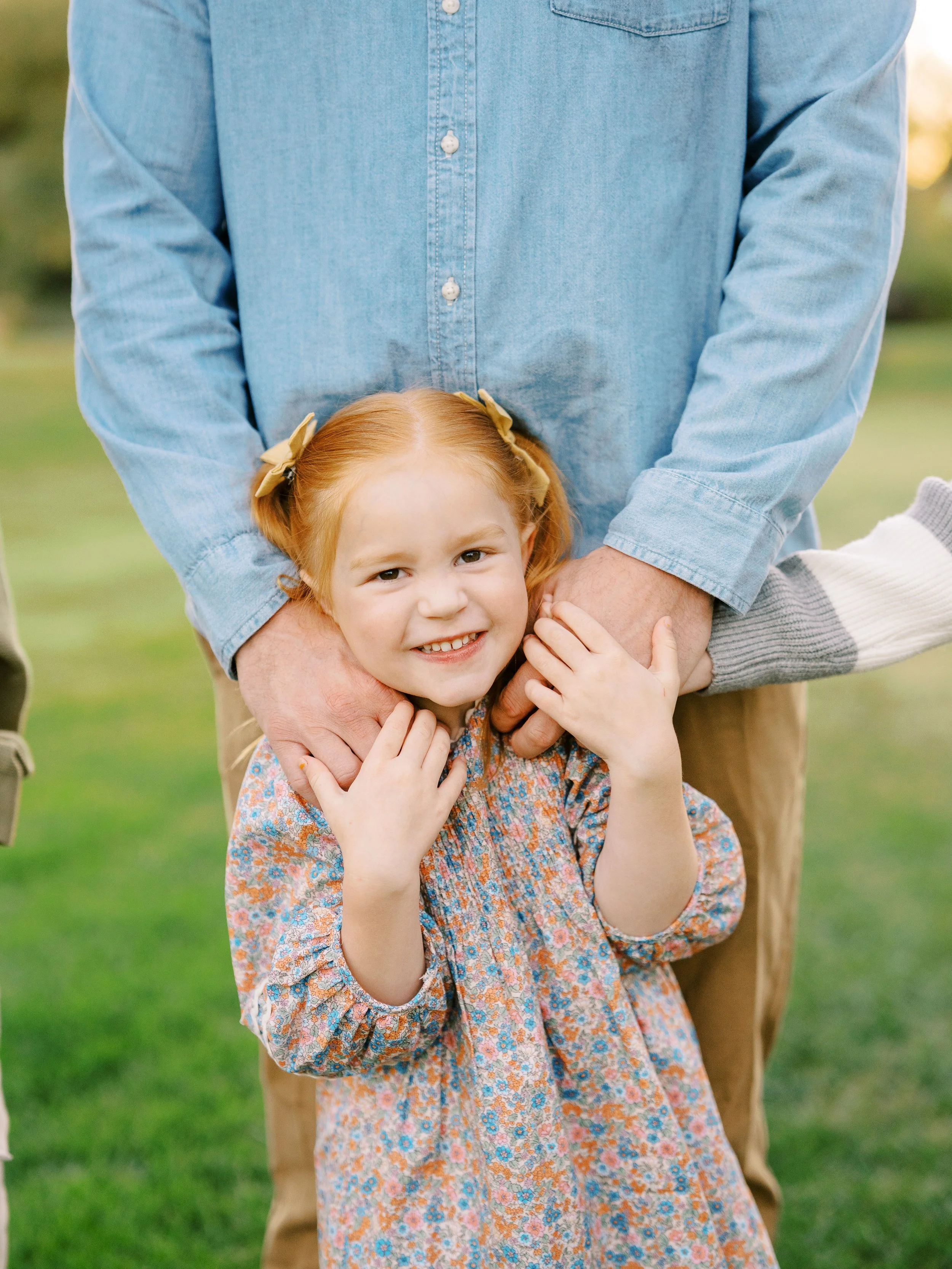 Young girl smiling between her father’s legs while holding his hands