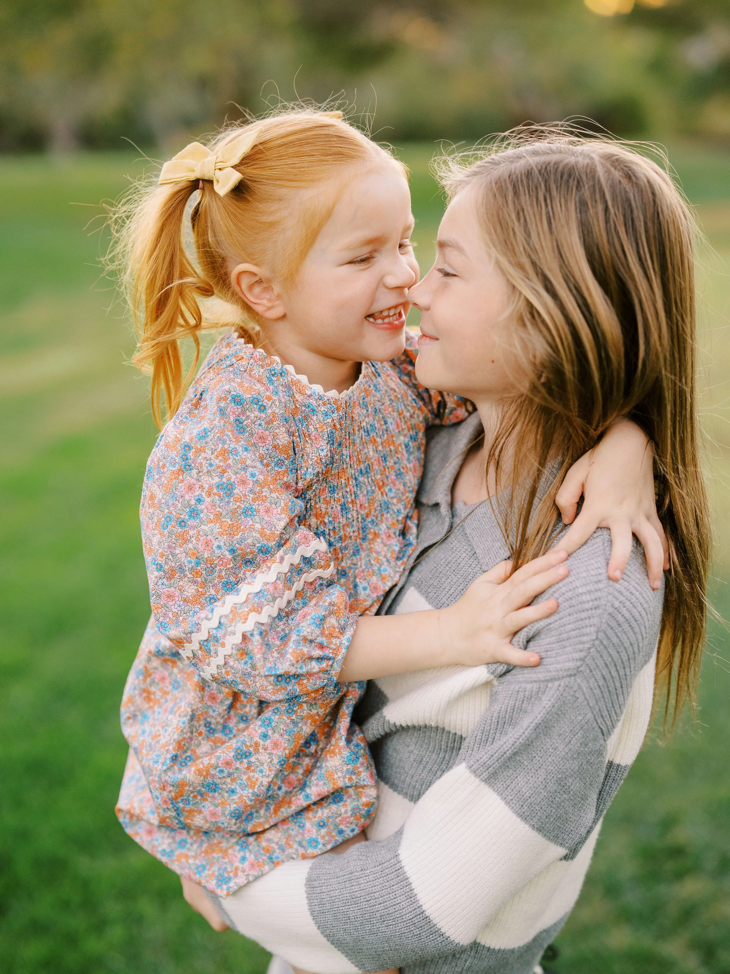Little sister leaning toward her older sister’s cheek as they hug