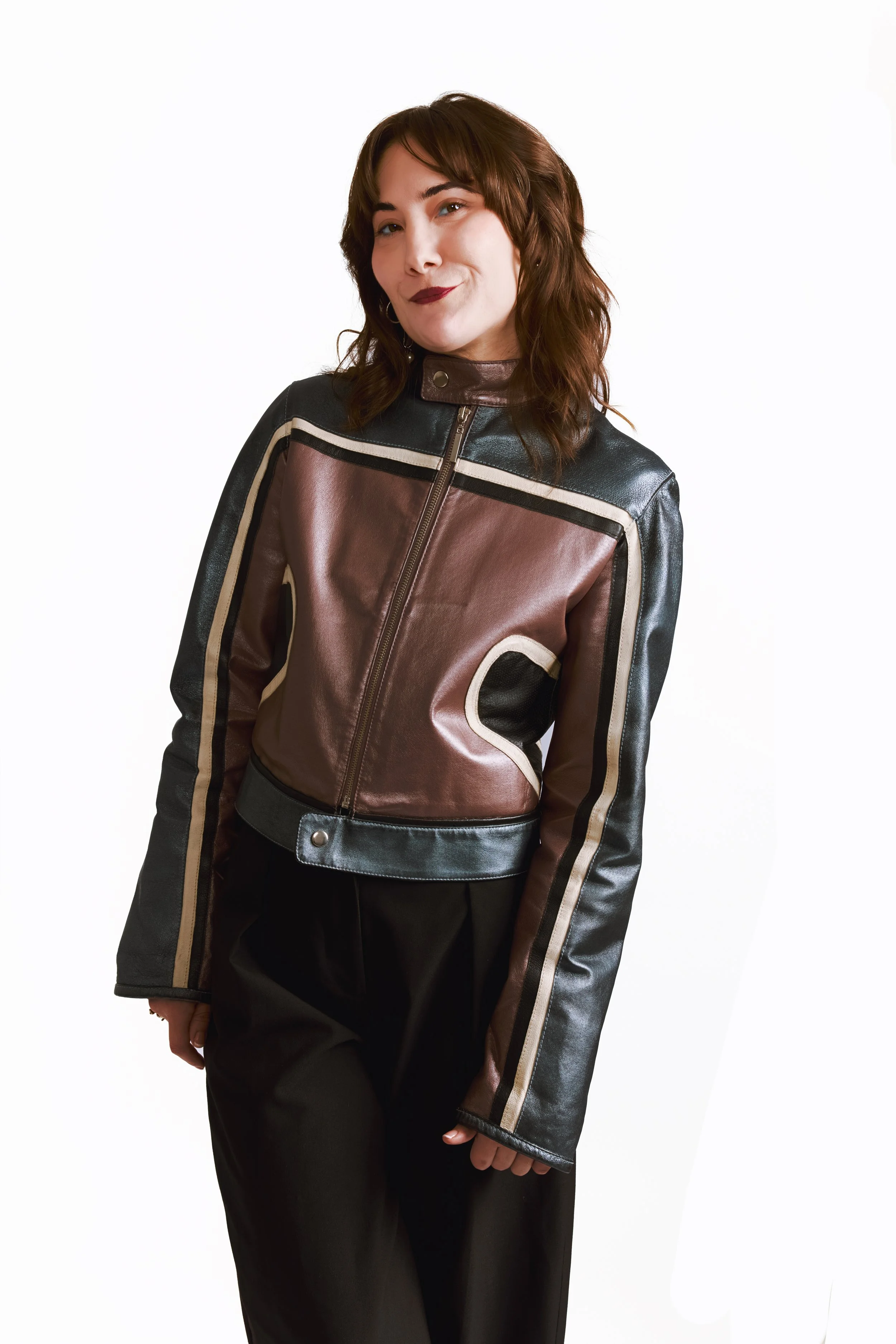 Sylvie Rubio, co-fondatrice de Care Care Agency. Jeune femme avec des cheveux ondulés bruns portant une veste en cuir marron et noire, souriant légèrement, posant contre un fond blanc.