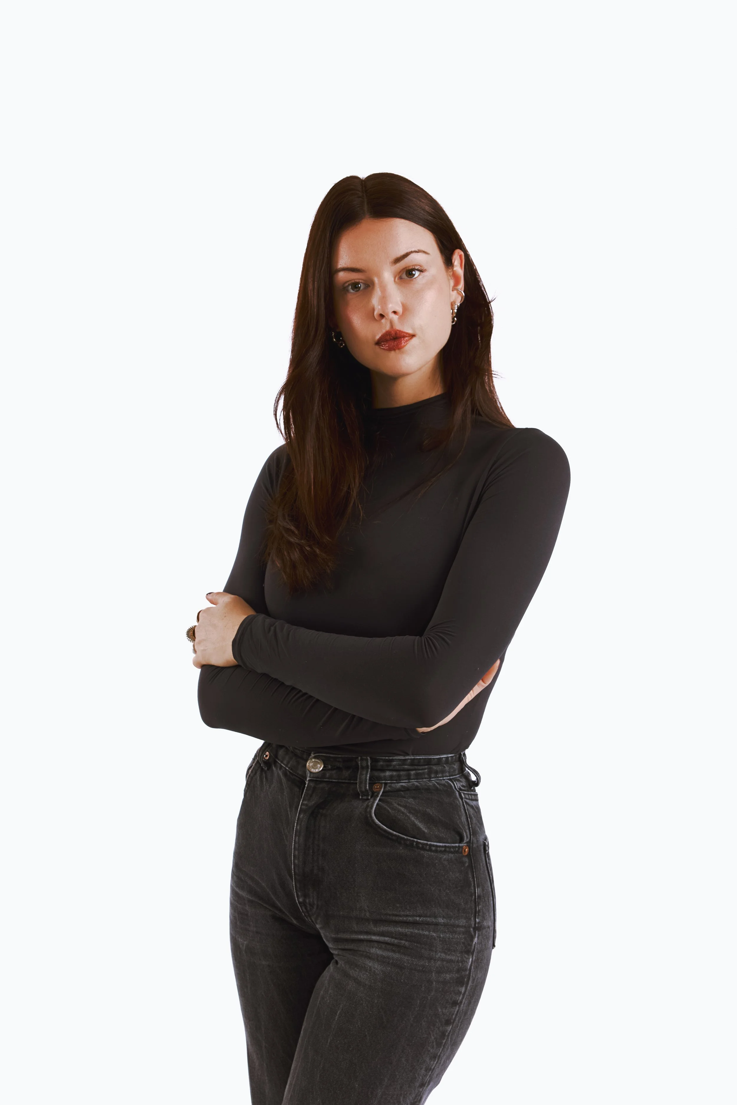 Félice Bricca, co-fondatrice de Care Care Agency. Jeune femme aux cheveux bruns, portant un haut noir à manches longues et un jean noir, posant avec les bras croisés contre un fond blanc.