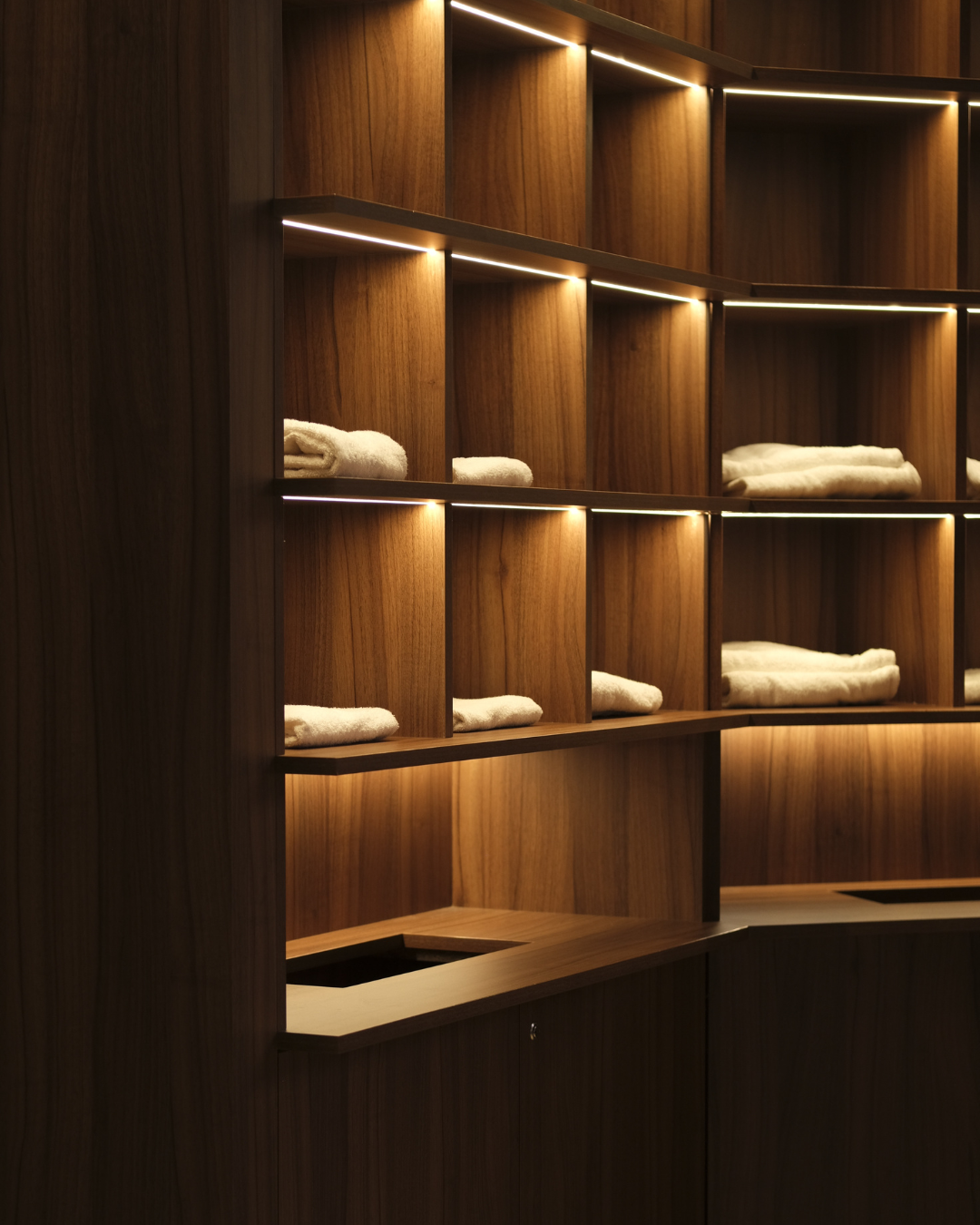 Vues d'une boutique Aesop avec étagères en bois avec des serviettes blanches pliées, éclairage intégré