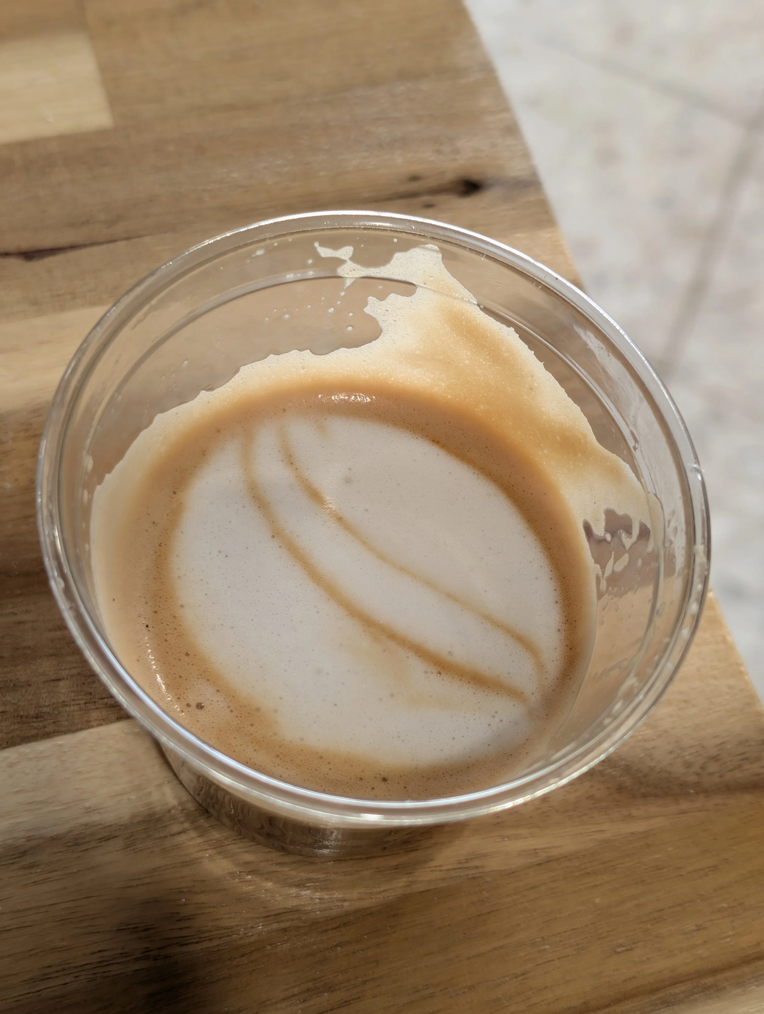 Close-up of a partially consumed iced coffee in a clear plastic cup on a wooden table.