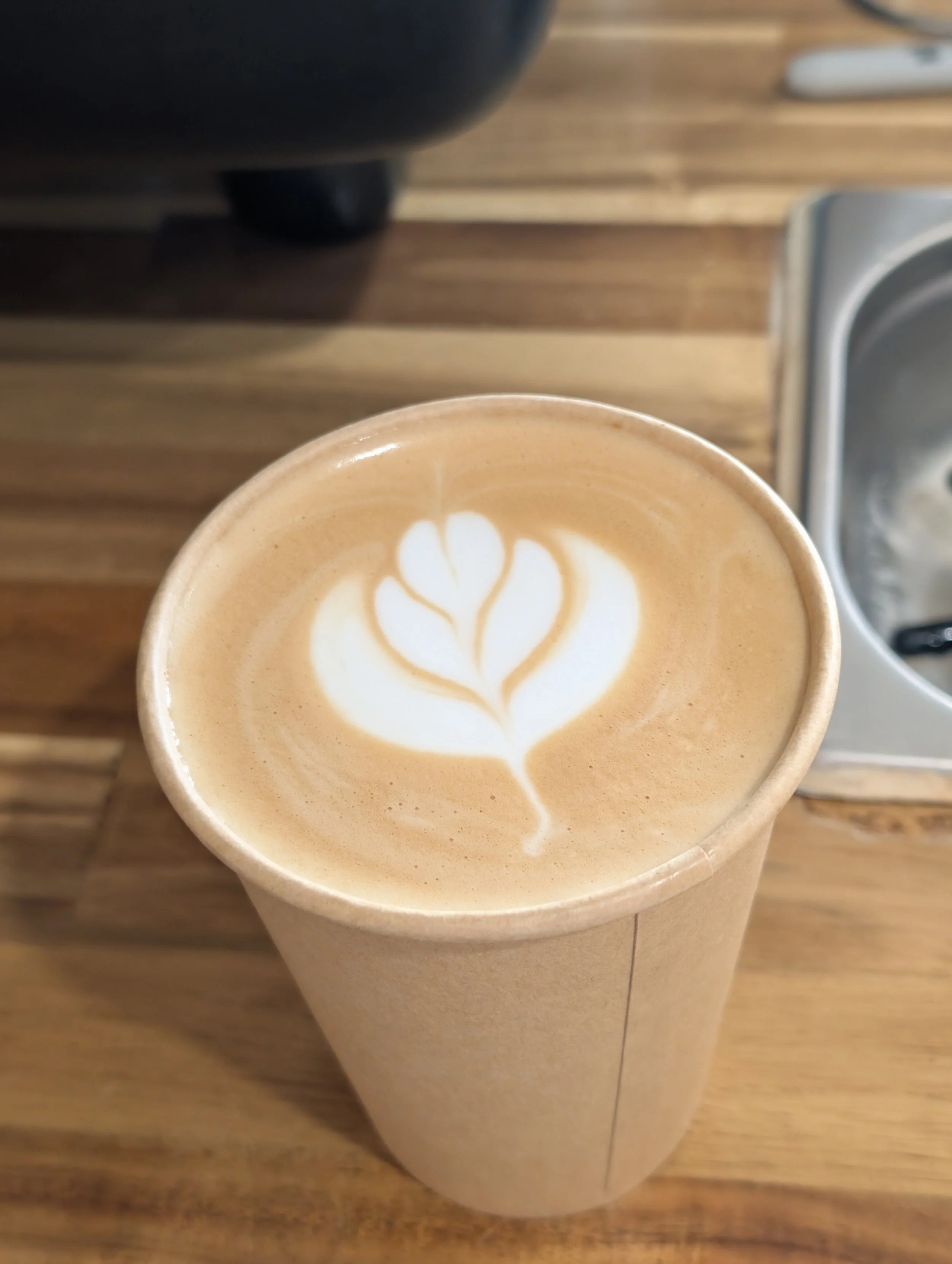 A cup of latte with a leaf-shaped foam art on top, on a wooden table.