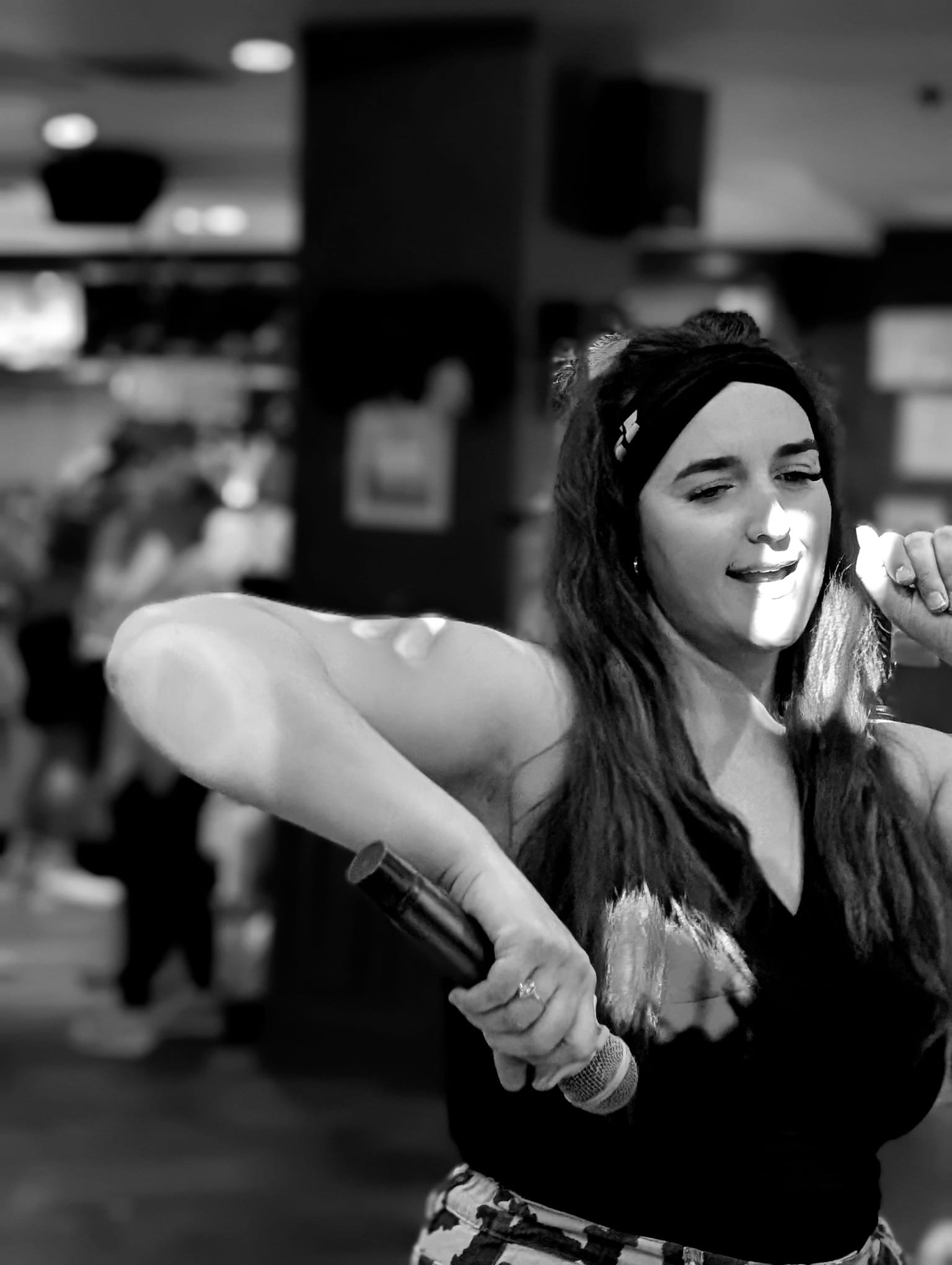 A black and white photo of Ceri-Ann, director of vibes really getting into a line dance to Texas Hold Em by Beyonce. She is throwing her arms in the air and showing everyone in the room a unique line dance.