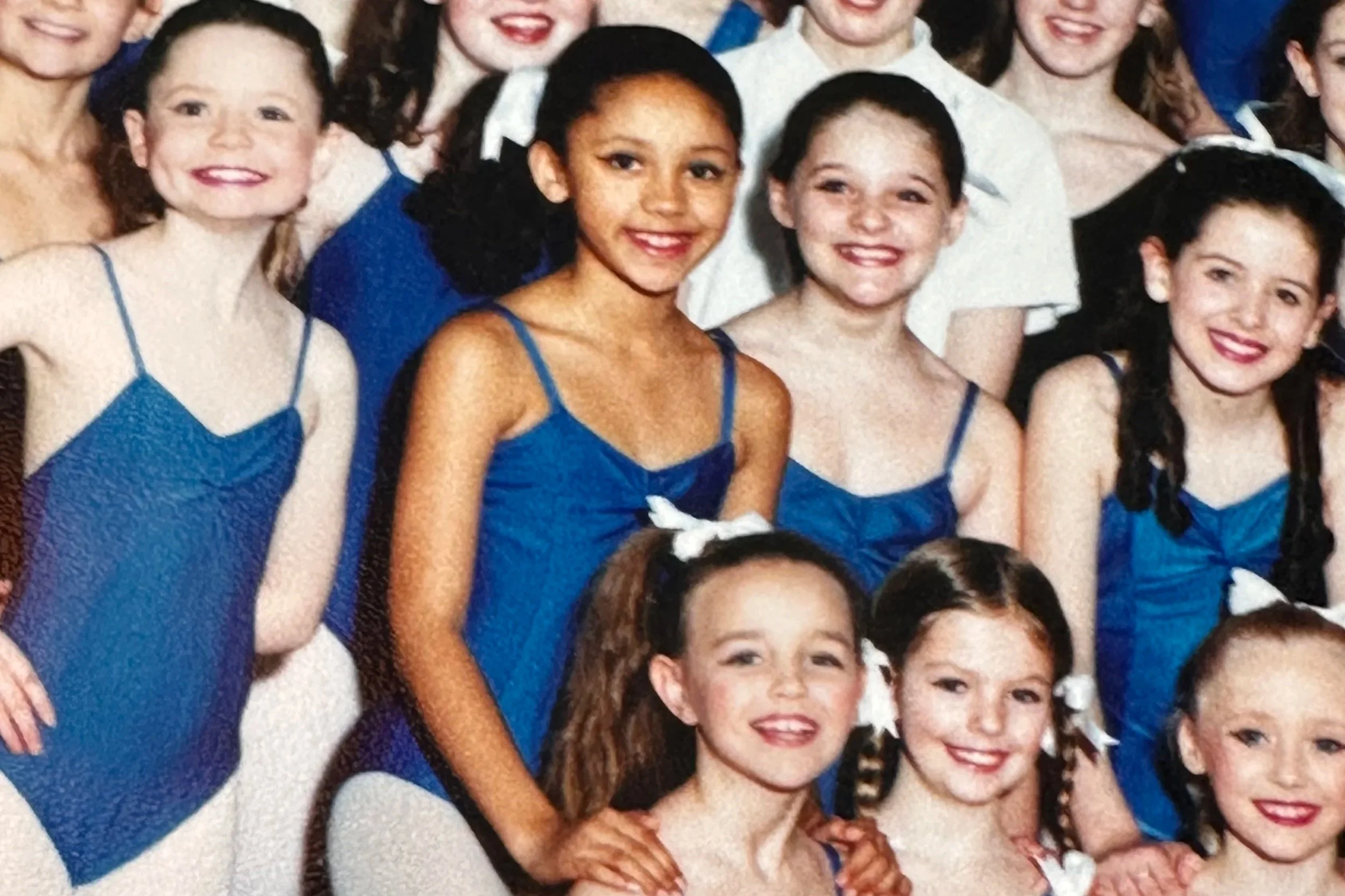 A group of young girls wearing blue dresses posing for a photo, smiling at the camera.