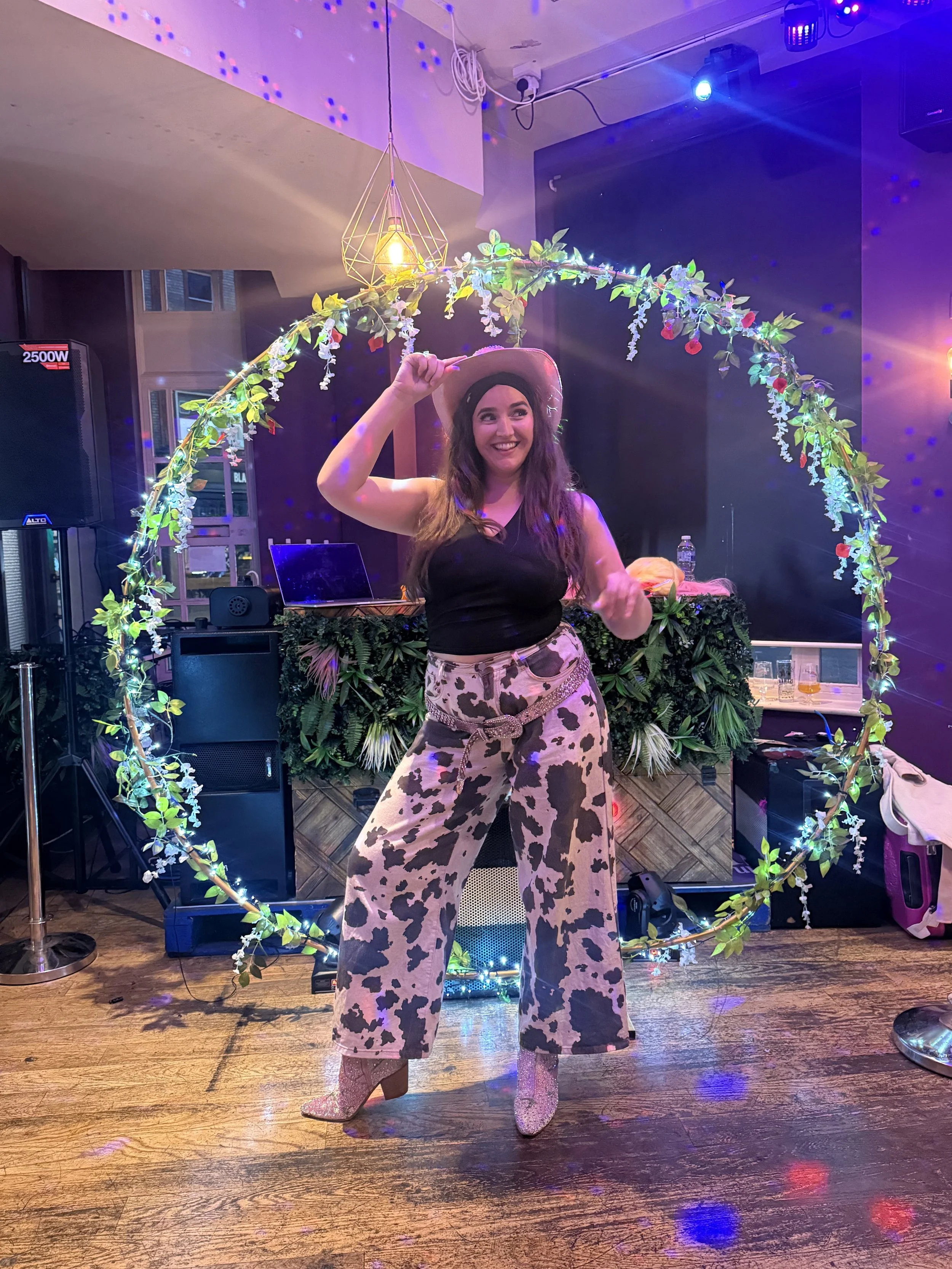 A colour photo of Ceri-Ann (director of vibes) at the signal box in Reading in  after a line dancing session where the energy is high. She is wearing cowgirl costume with cow print trousers and her pink dazzling shoes, hat and belt.