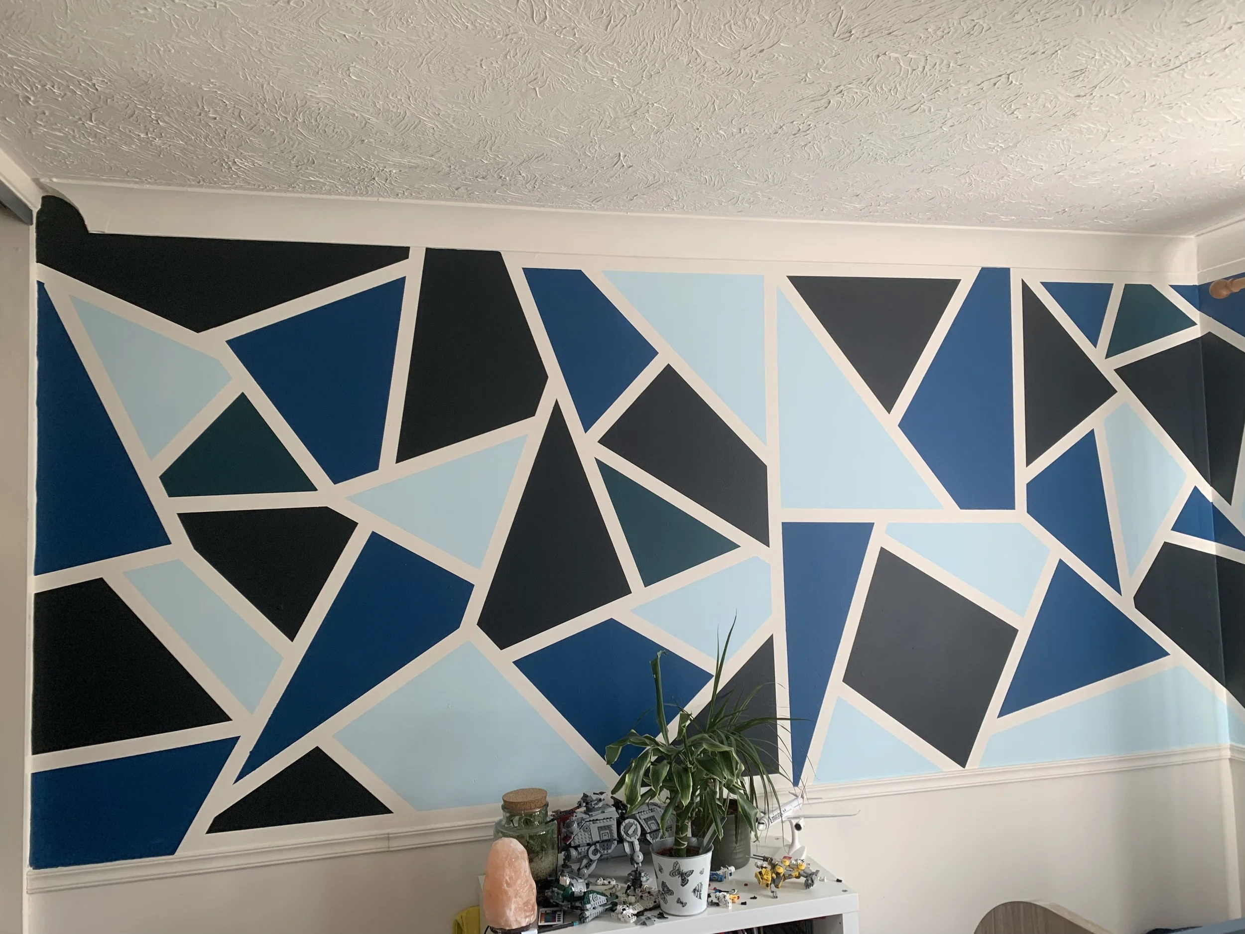 Child's bedroom wall in a graphic design. Frog tape and Valspar tester pots in various bright and dark shades of blue to personalise the bedroom.